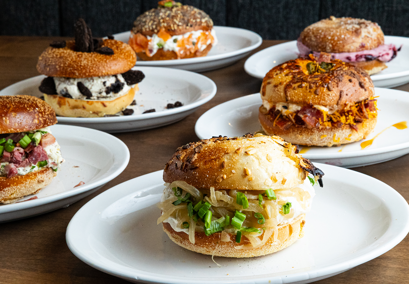 The Delicatessen: Six plates of gourmet sandwiches with various toppings, served on white dishes on a wooden table.