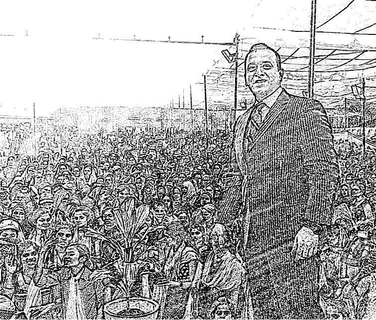 A man in a suit standing in front of a large crowd of people, with some industrial structures visible in the background.