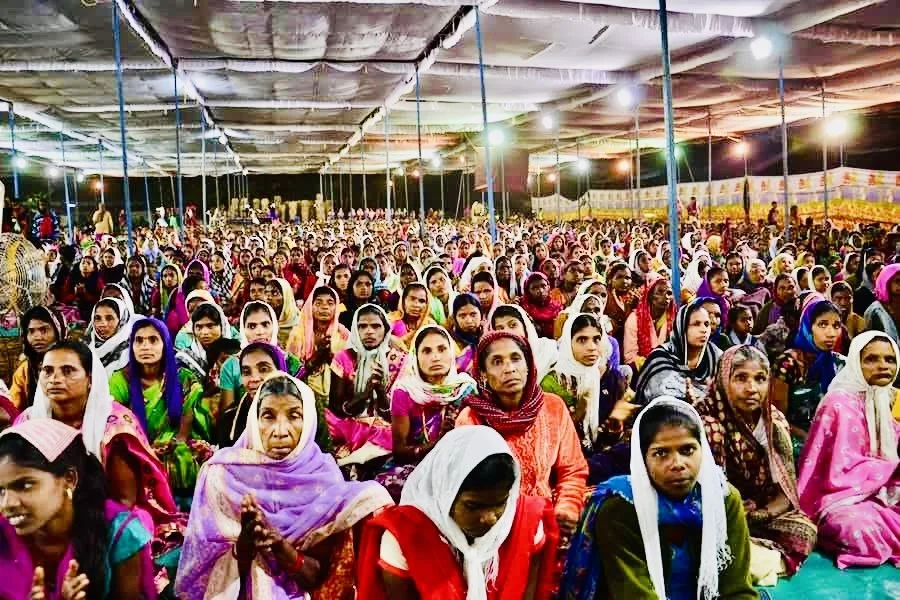 A large gathering of women seated under a tent at night, attending an event.