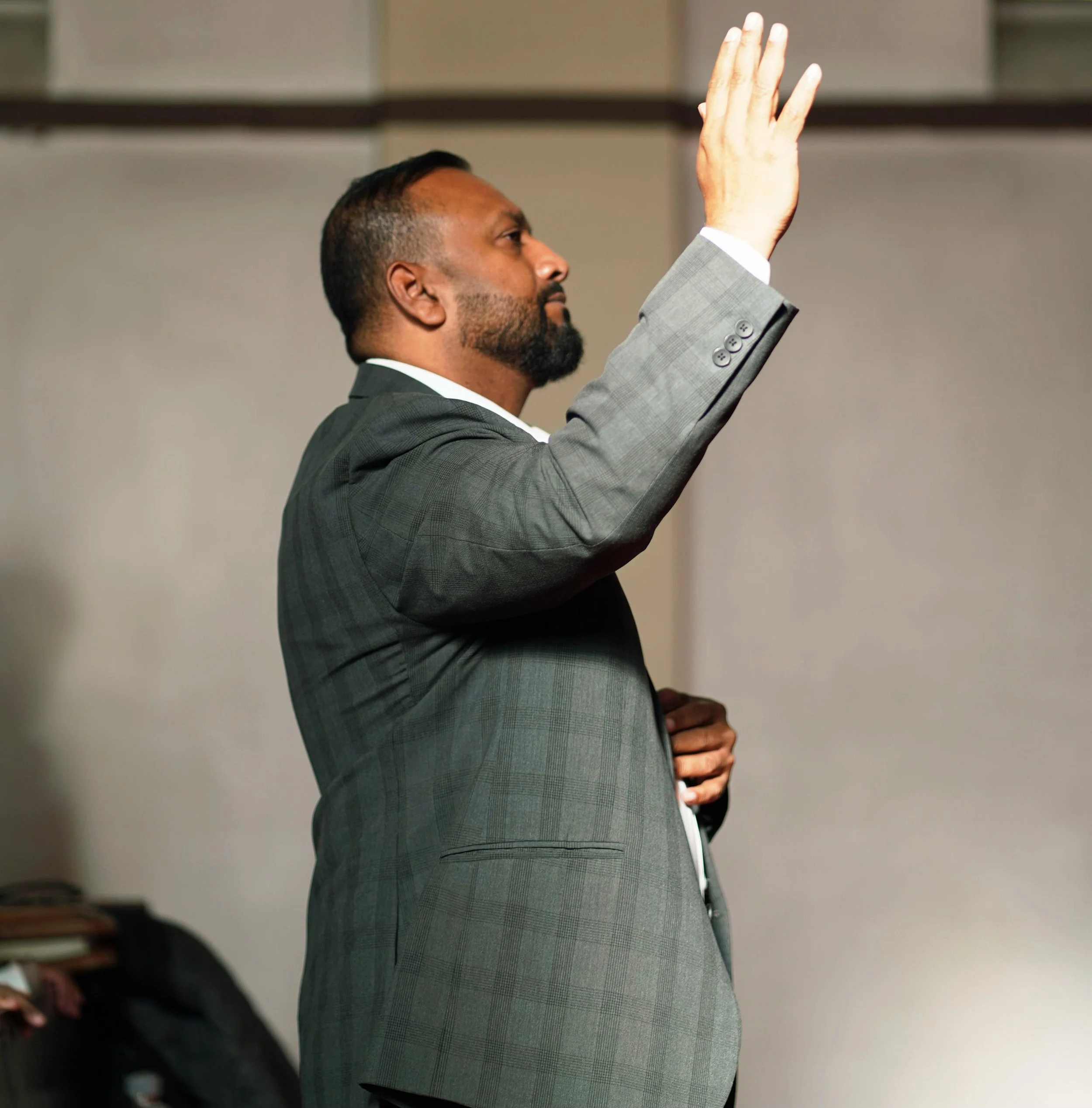 A man in a gray suit raising his right hand during what appears to be a formal or official setting.