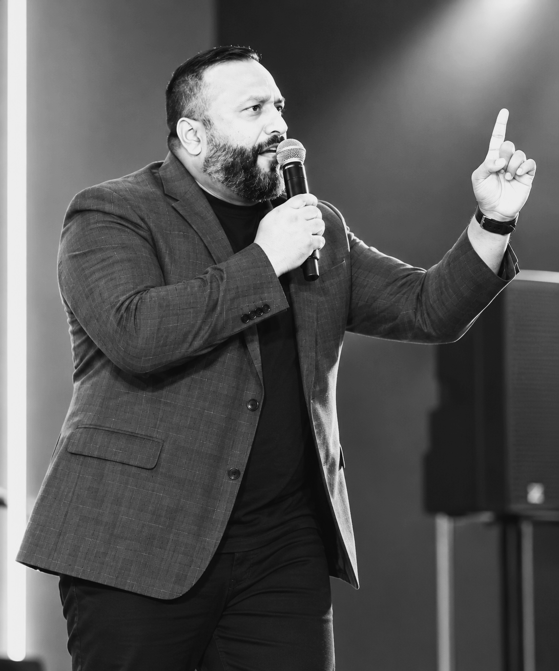 Man with beard in suit speaking into microphone and gesturing with his right hand.