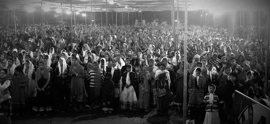 Large crowd of women and children gathered under a tent.