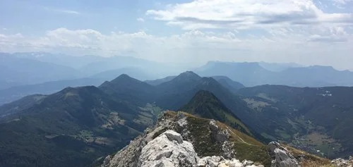 Vue panoramique de monts et vallées depuis une crête de montagne, nuages dans le ciel.