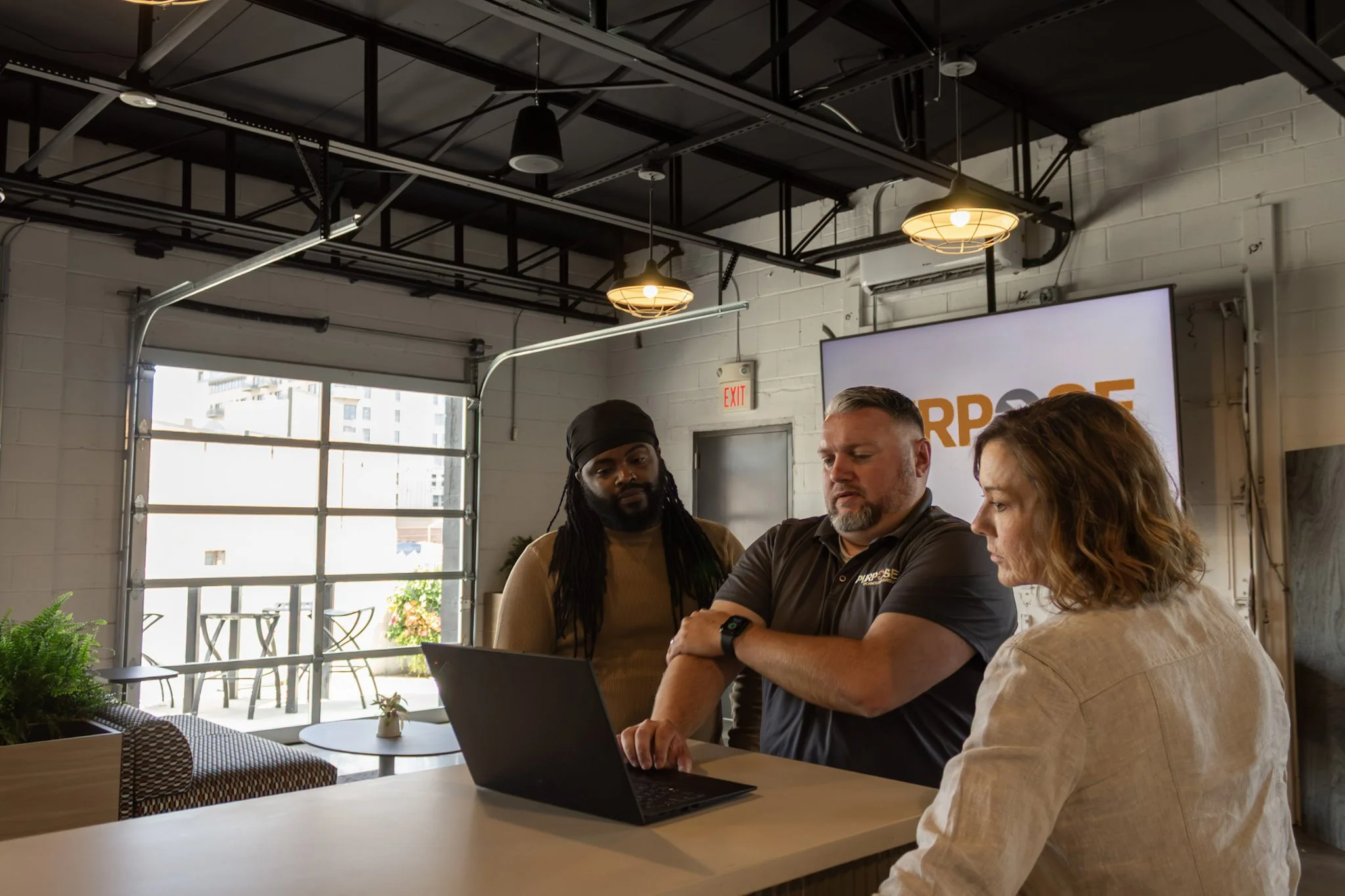 An image of a team of three people around a laptop to illustrate fully managed technology services with Purpose Technology Group