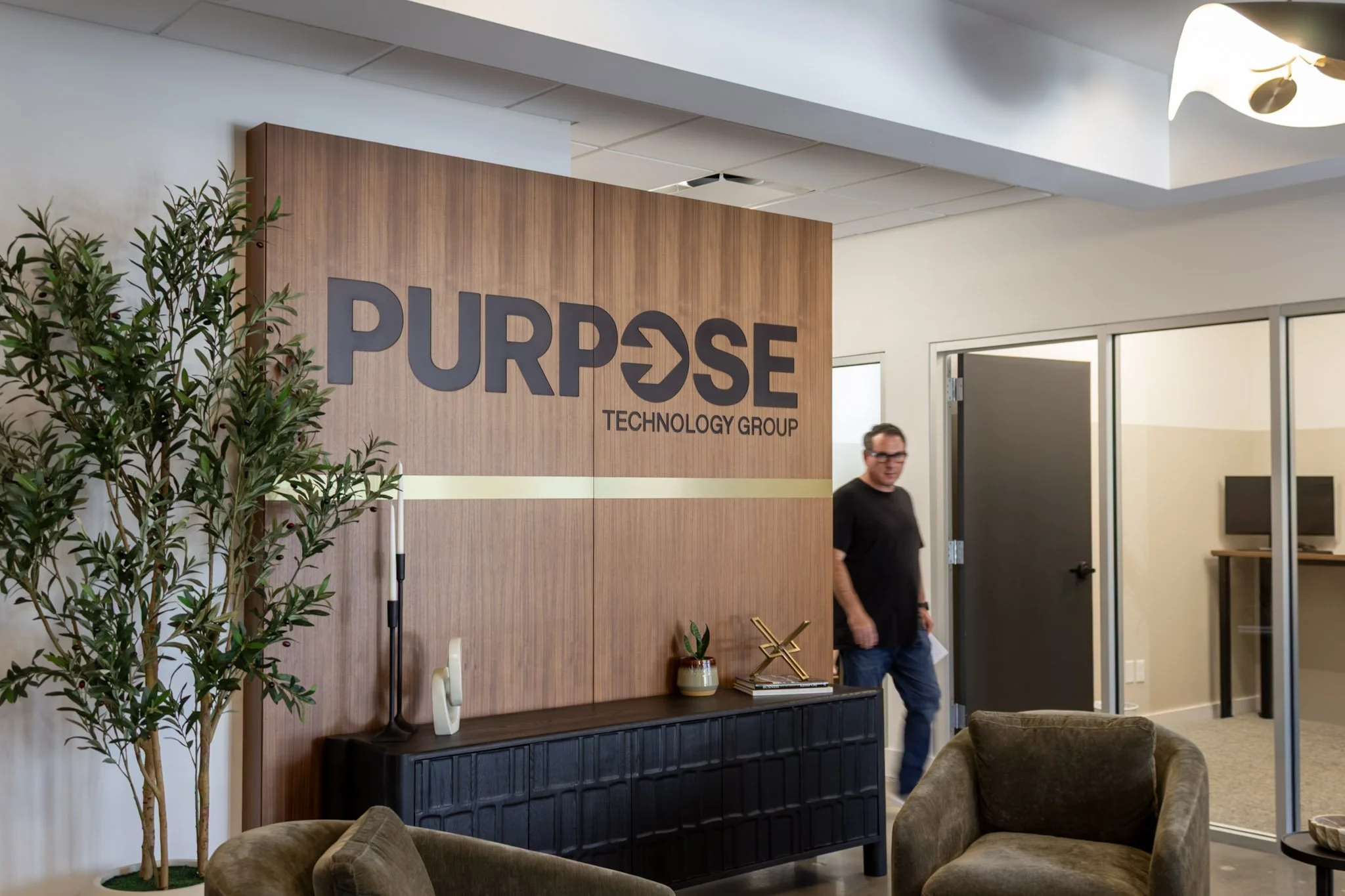 A person walking in an office setting by a sign with Purpose Technology Group carved in wood.