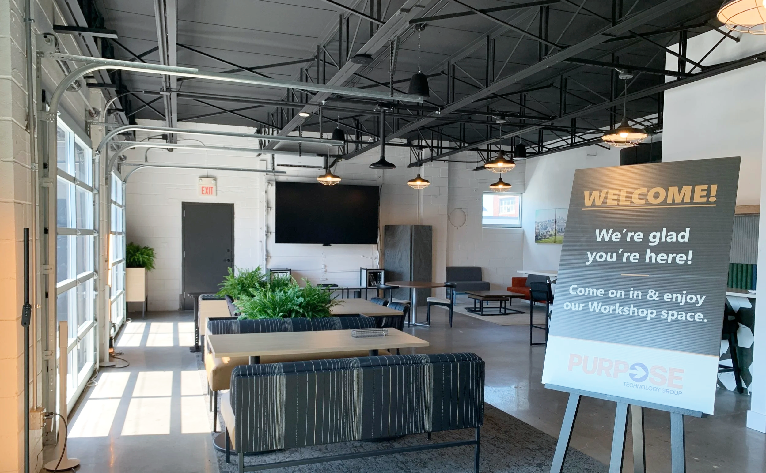 Photograph of a modern office event space with garage doors that open to a patio and a welcome sign saying we're glad you're here!