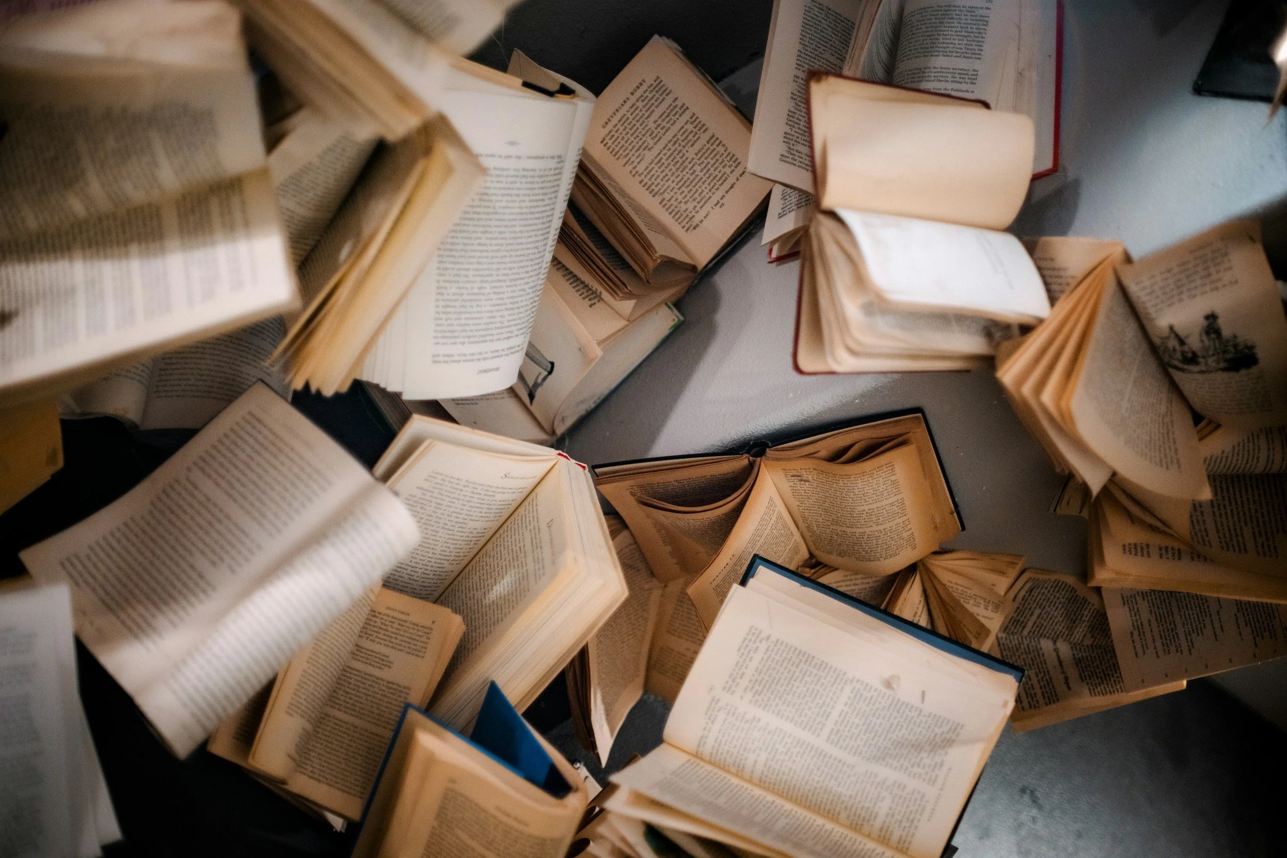 A pile of open books and magazines scattered on a surface, viewed from above.