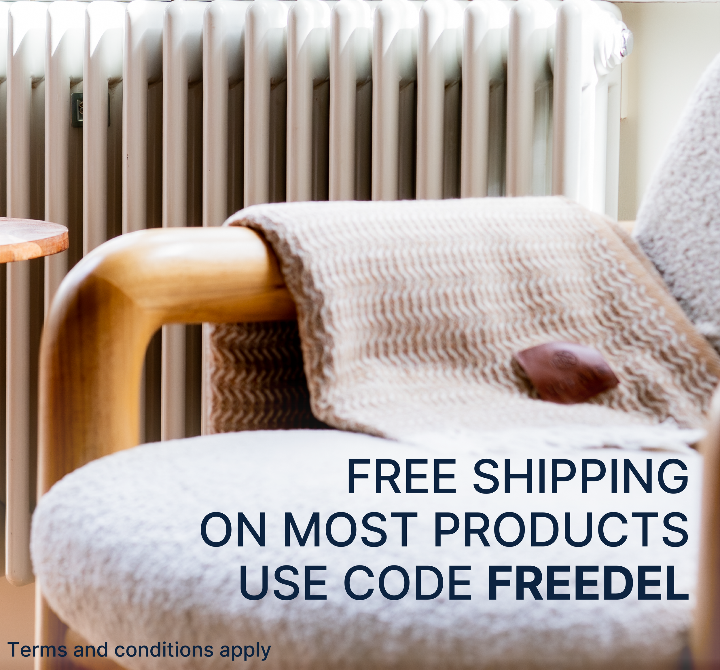 Close-up of a cushioned armchair with a blanket draped over the armrest, in front of a vintage radiator and part of a poster or sign with text about free shipping and promo codes.