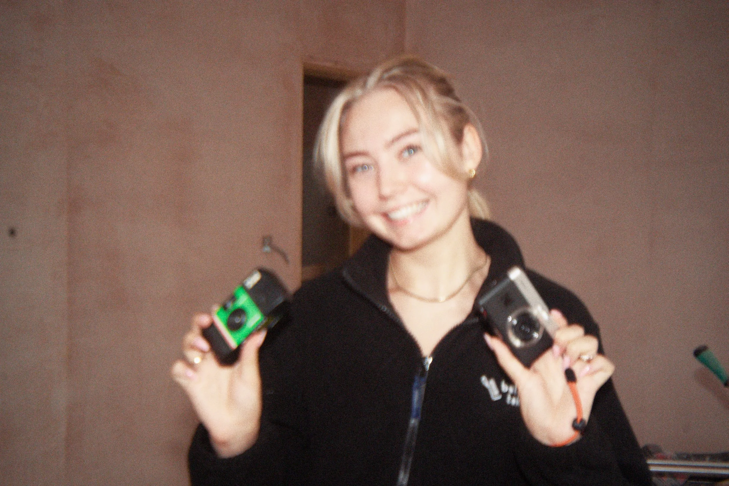 A woman smiling and holding several small cameras, some with colored accents, and looking at the camera.