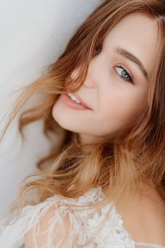 A smiling young woman with long, wavy, red hair and blue eyes, looking slightly to the side.