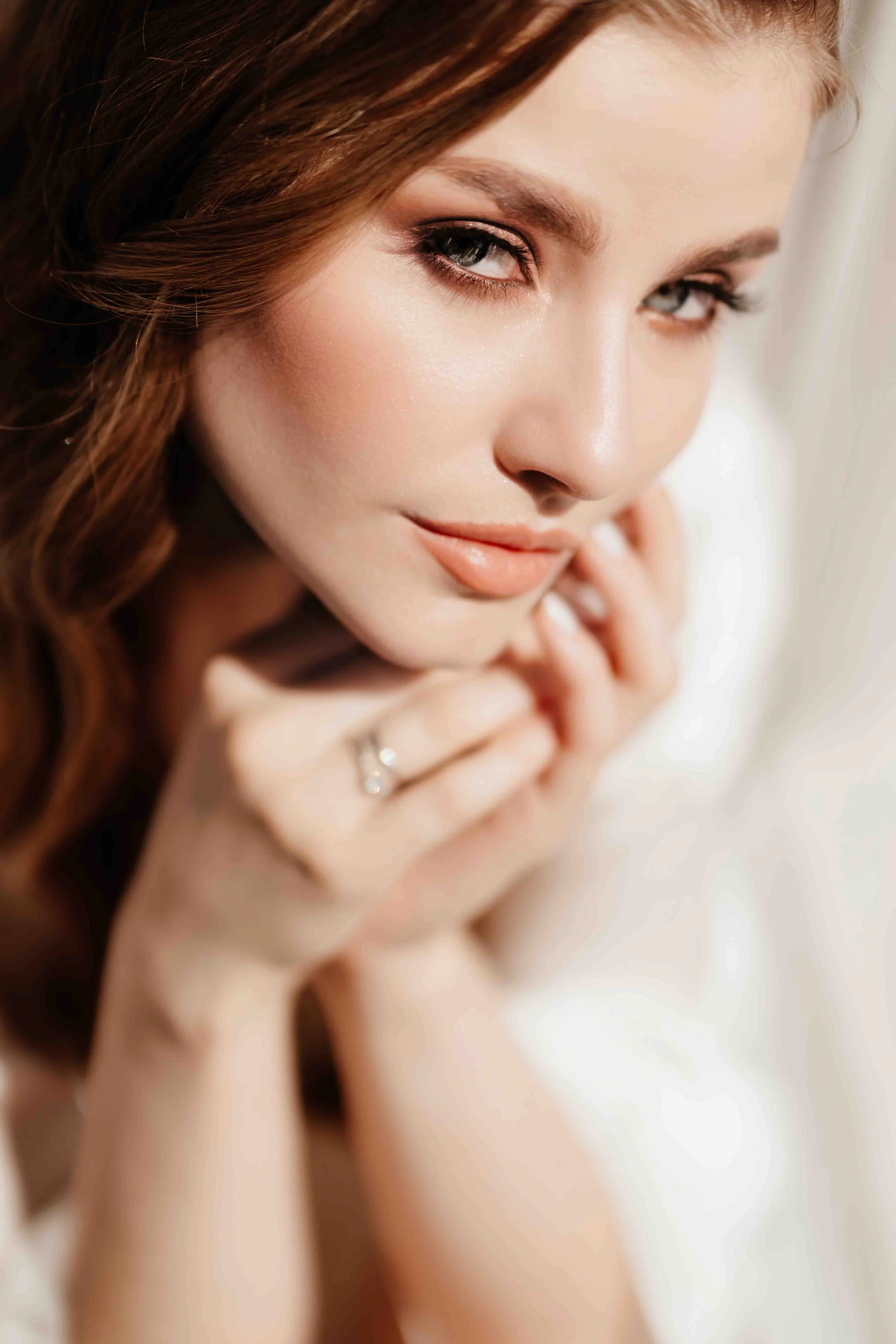 Close-up of a woman with light skin, auburn hair, and light makeup, resting her head on her hands.