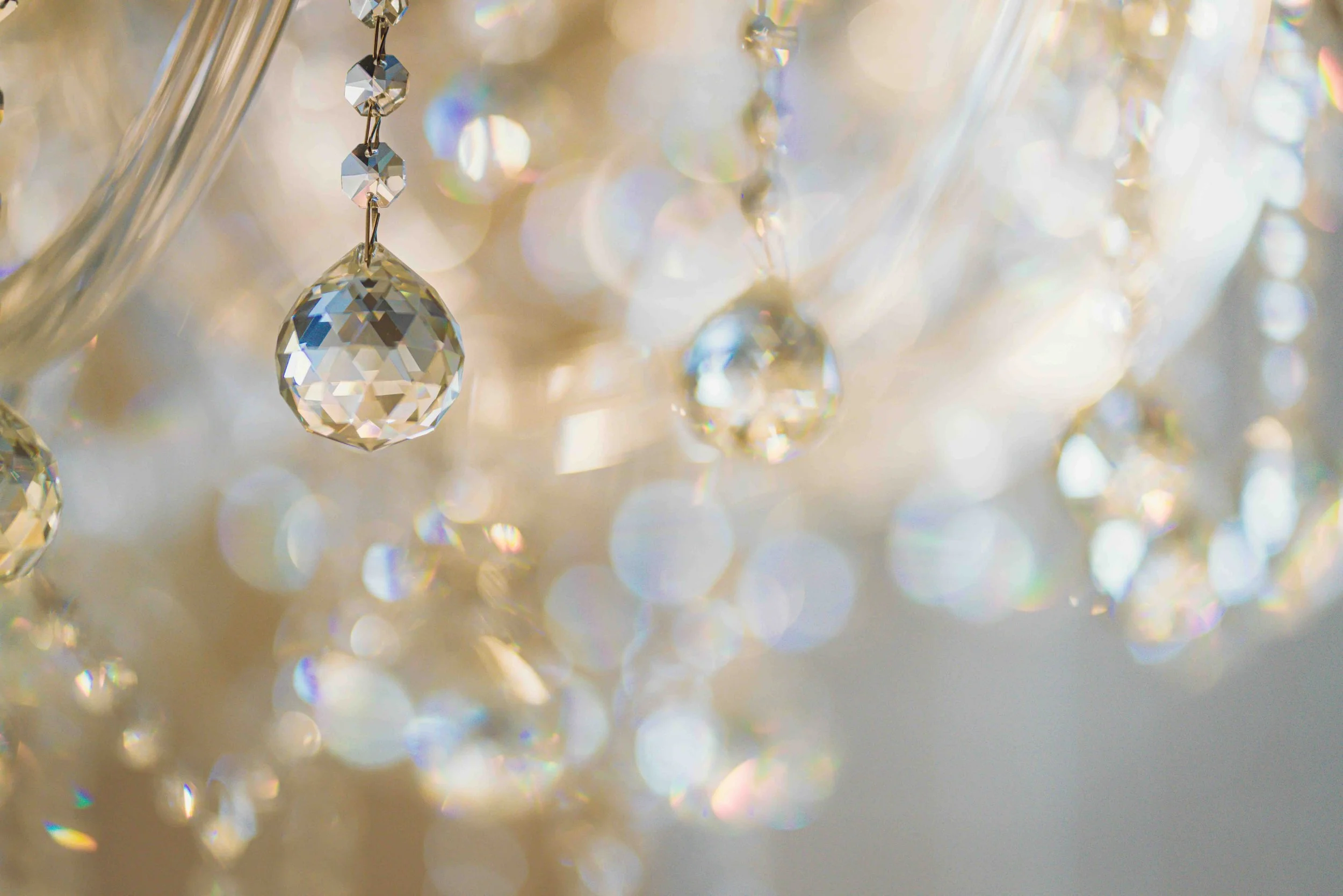 Close-up of a chandelier with hanging crystal prisms reflecting light and creating colorful bokeh effects in the background.