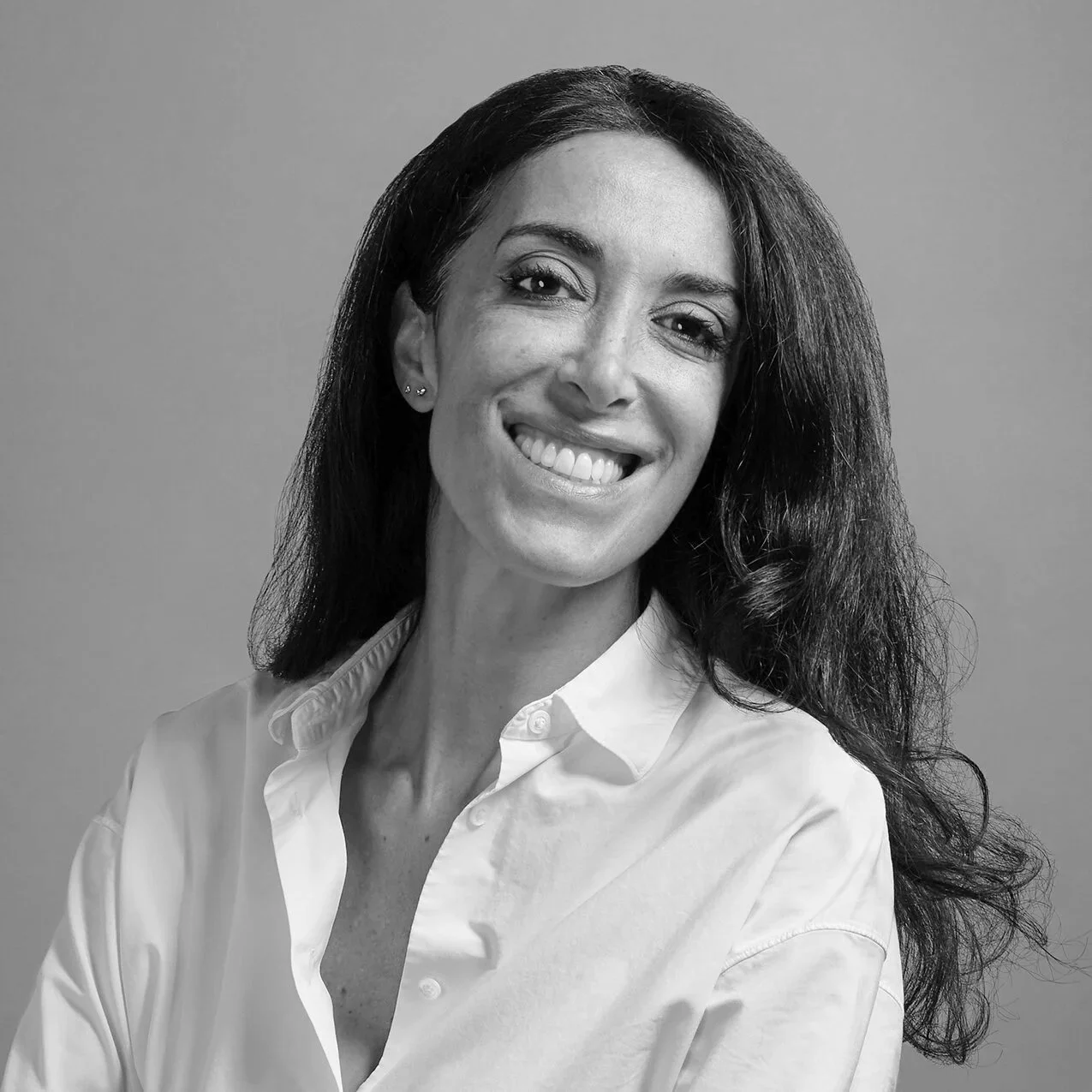 Black and white portrait of a woman with long, curly hair, smiling, wearing a white button-up shirt, against a plain background.