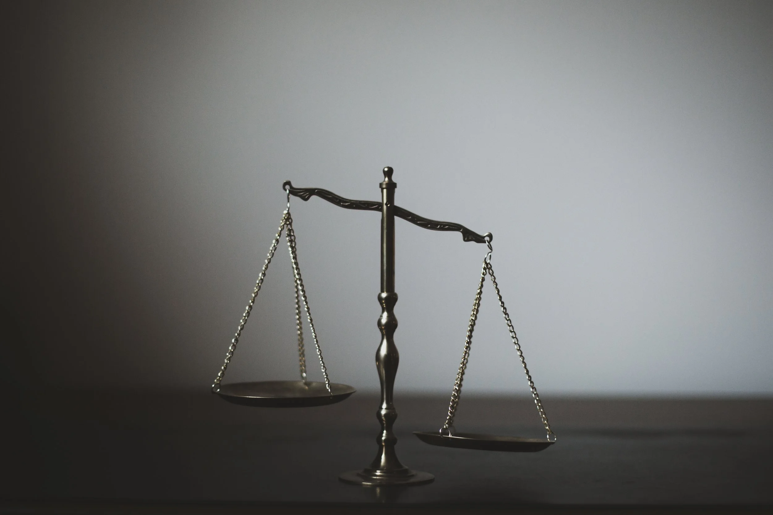 A metallic balance scale with empty trays, centered on a dark surface against a plain gray background.