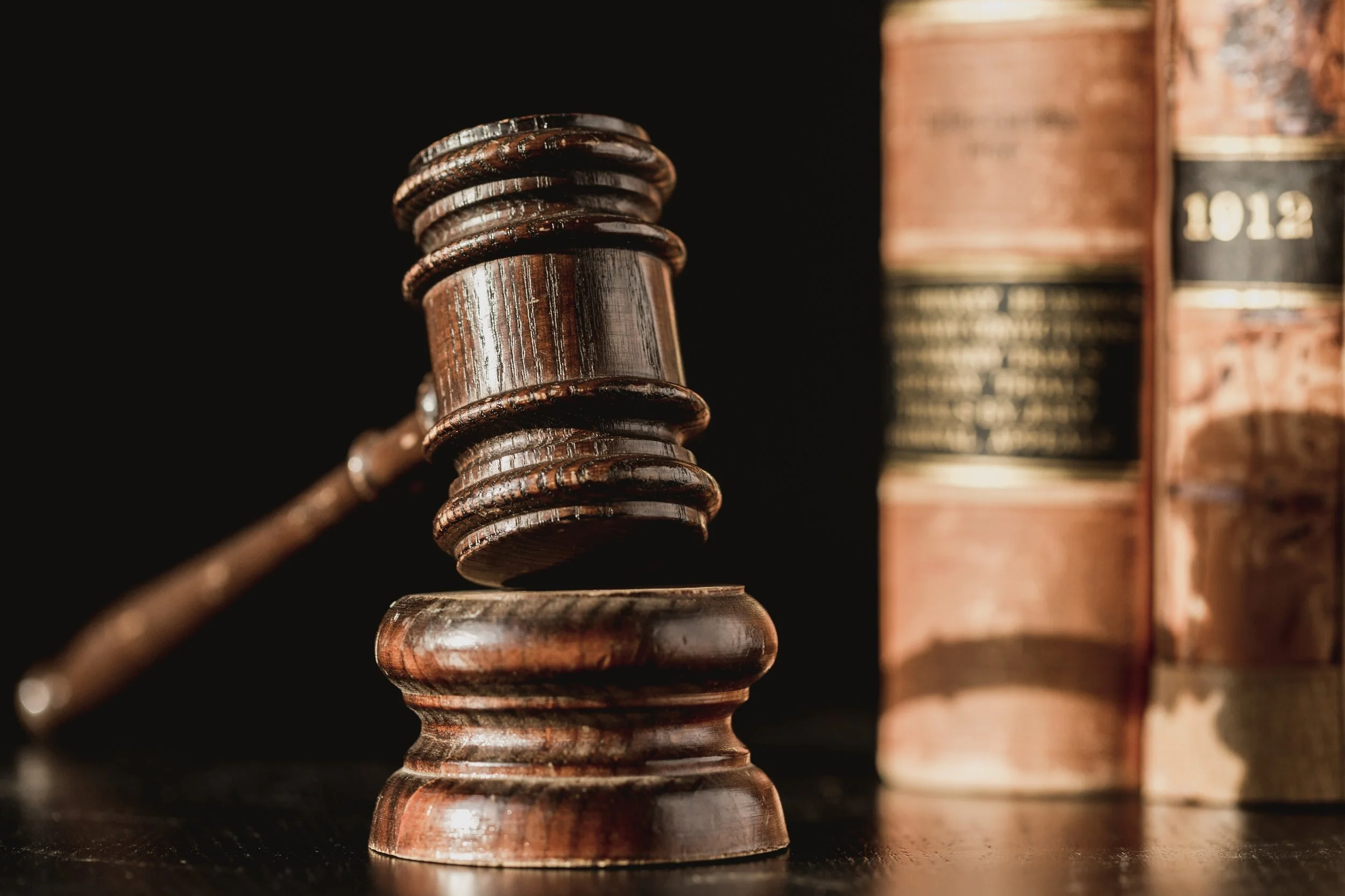 Close-up of a wooden gavel on a dark surface with books in the background.