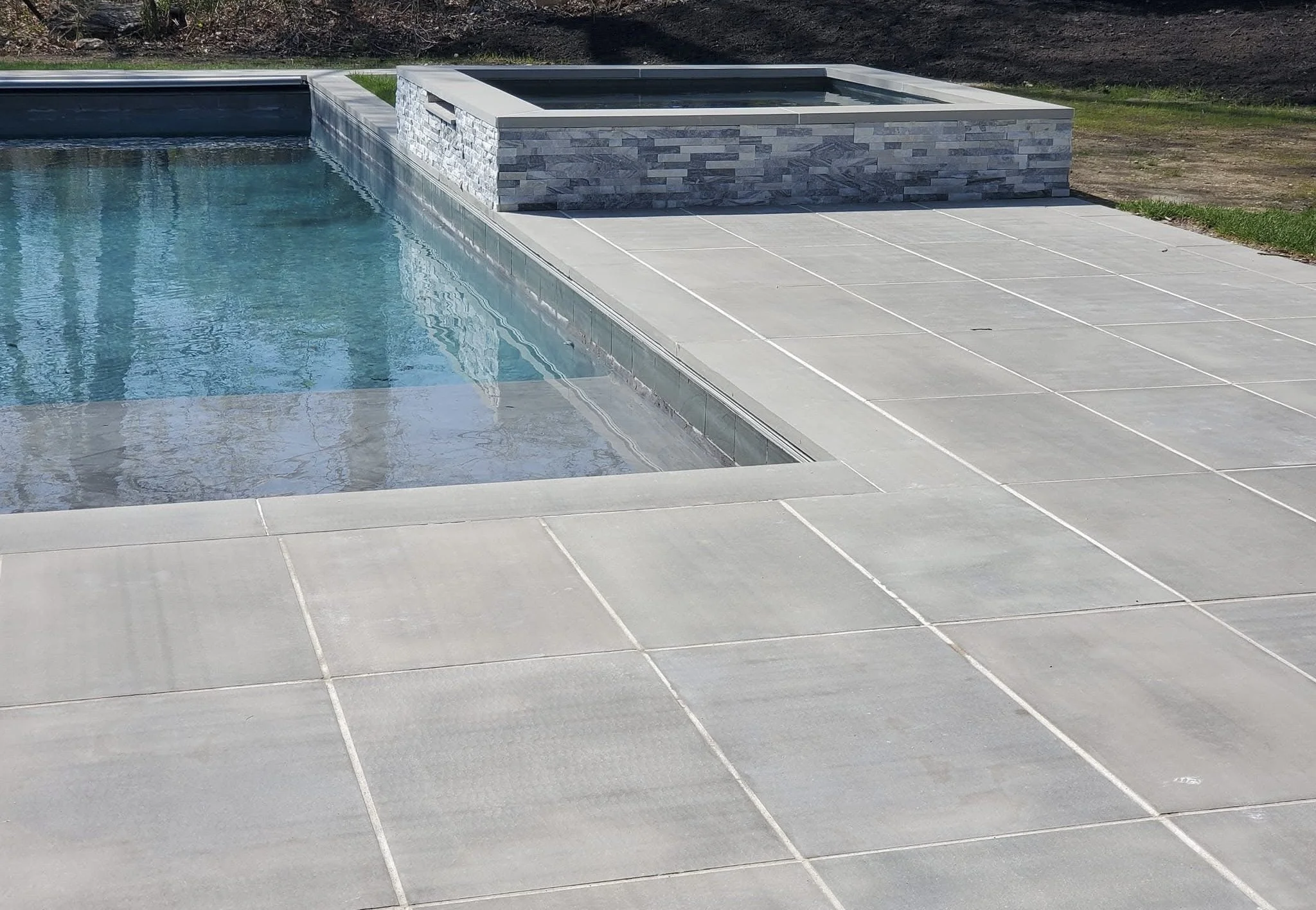A rectangular swimming pool with light gray tile surround and a raised hot tub with gray stone exterior.