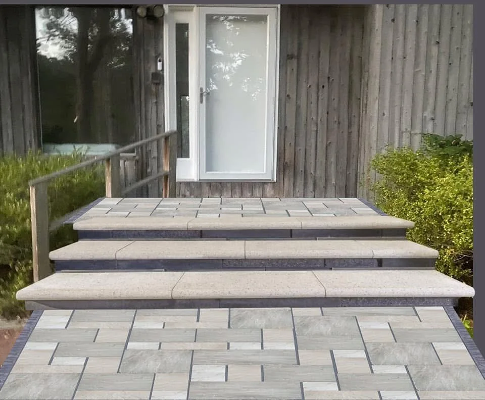 Outdoor wooden steps with stone-tile landing leading to a white door on a wooden house, with green bushes on the right.