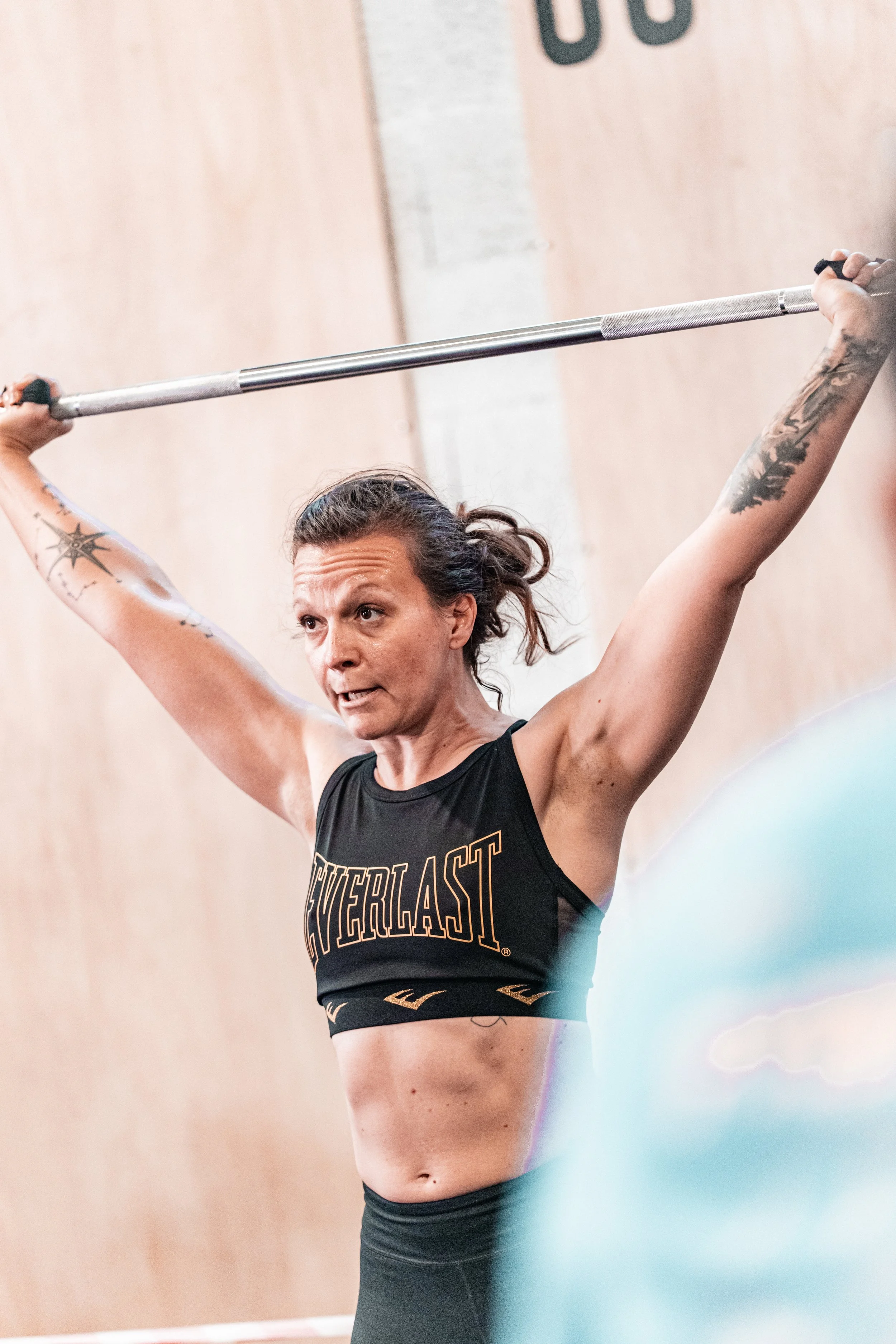 Une femme athlétique soulève une barre d'haltérophilie en maîtrisant une posture d'entraînement, portant un débardeur noir avec le logo Everlast.