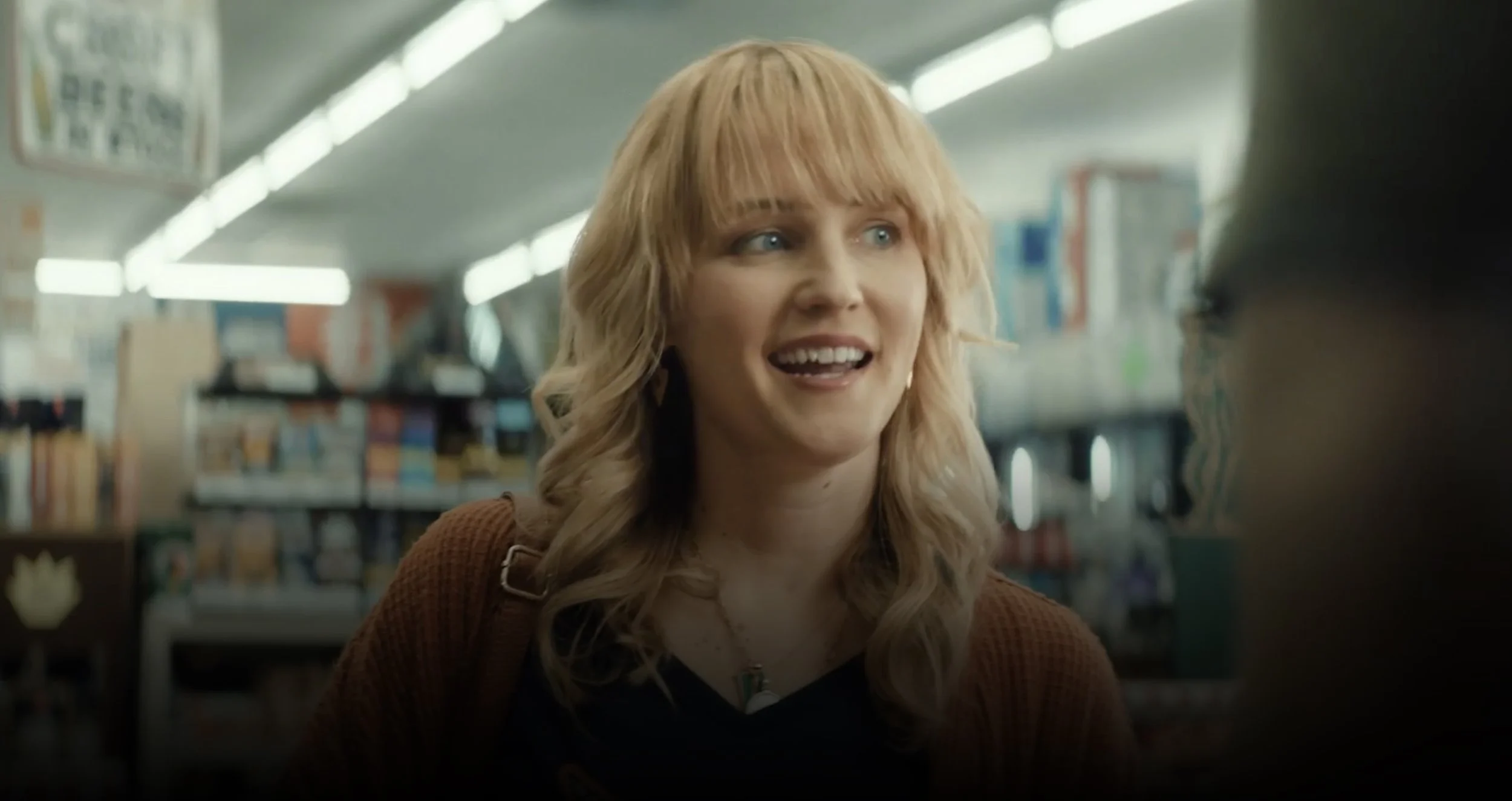 A blond woman in a corner store buying a lottery ticket.