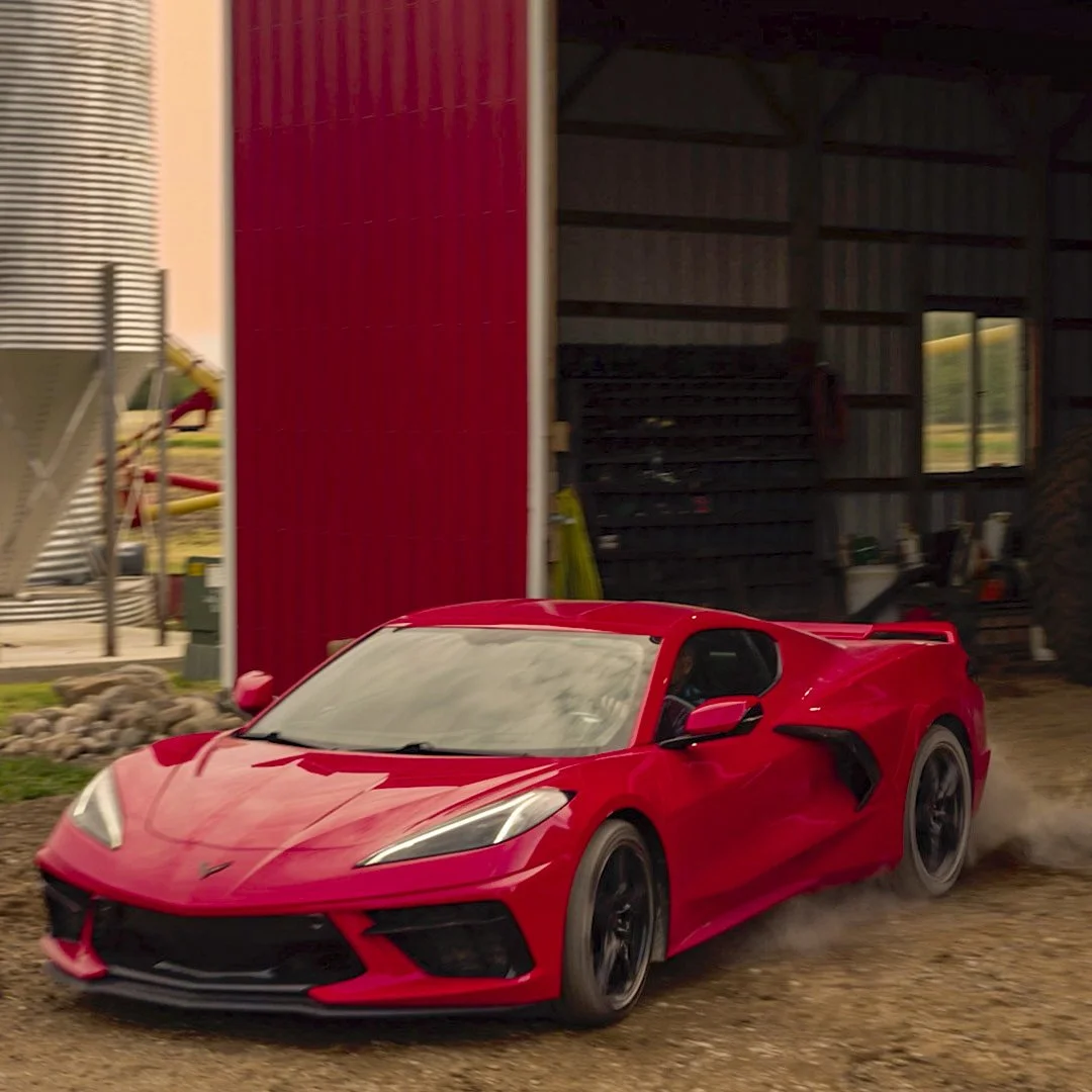 A still from a commercial of a red Corvette driving out of a red barn.