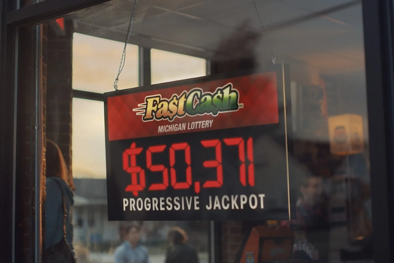 A convenience store window showing a Michigan Lottery Fast Cash progressive jackpot.