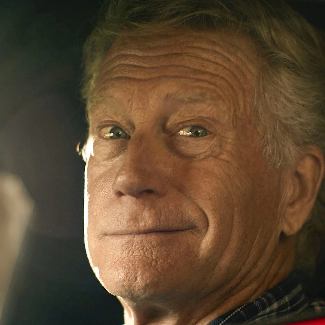 A still from a commercial of a farmer smiling at the camera from inside a sports car.