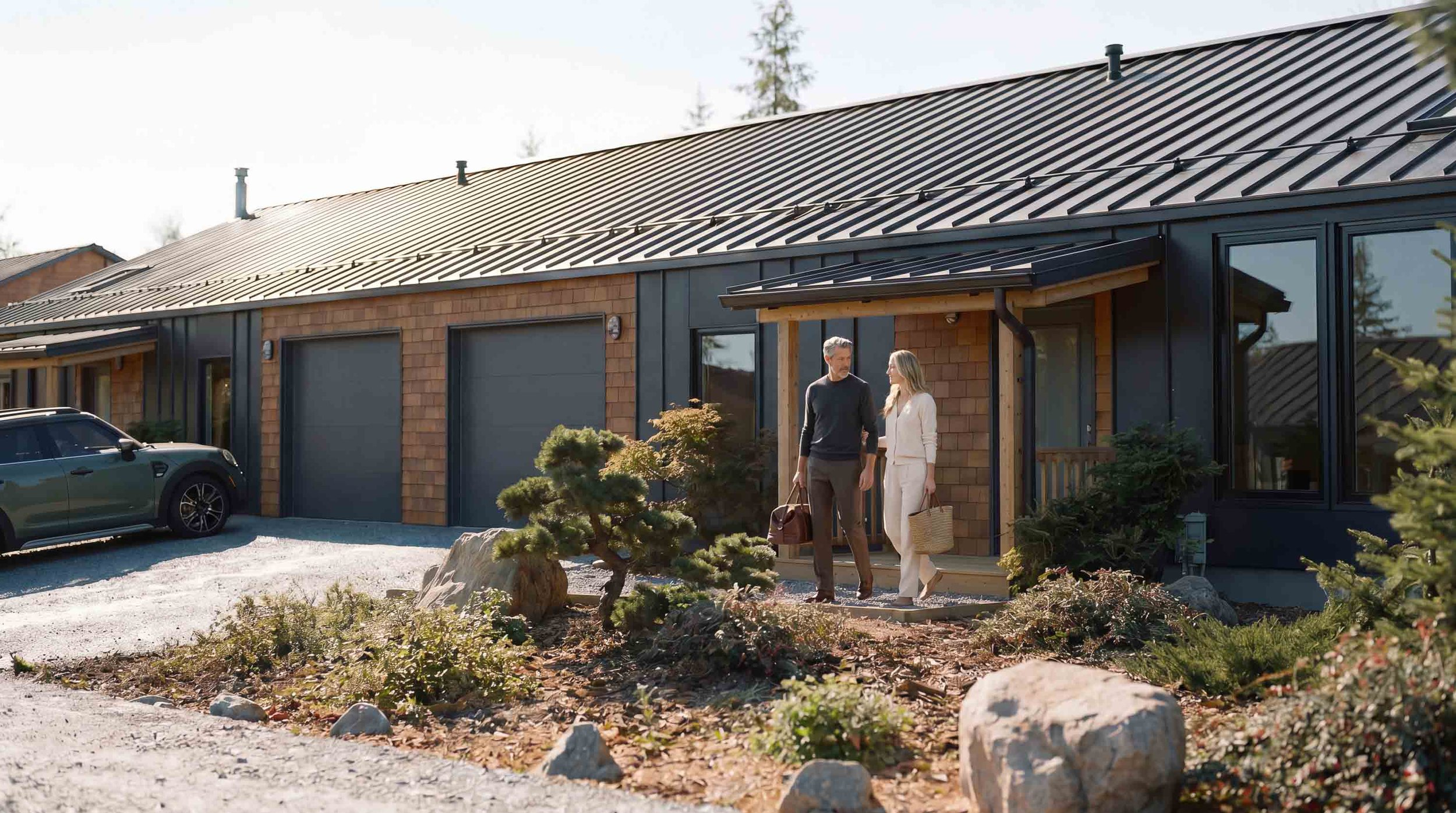 A couple walk out of a modern Nova Scotia home with a black metal roof, wooden tile and black metal siding, and large windows.