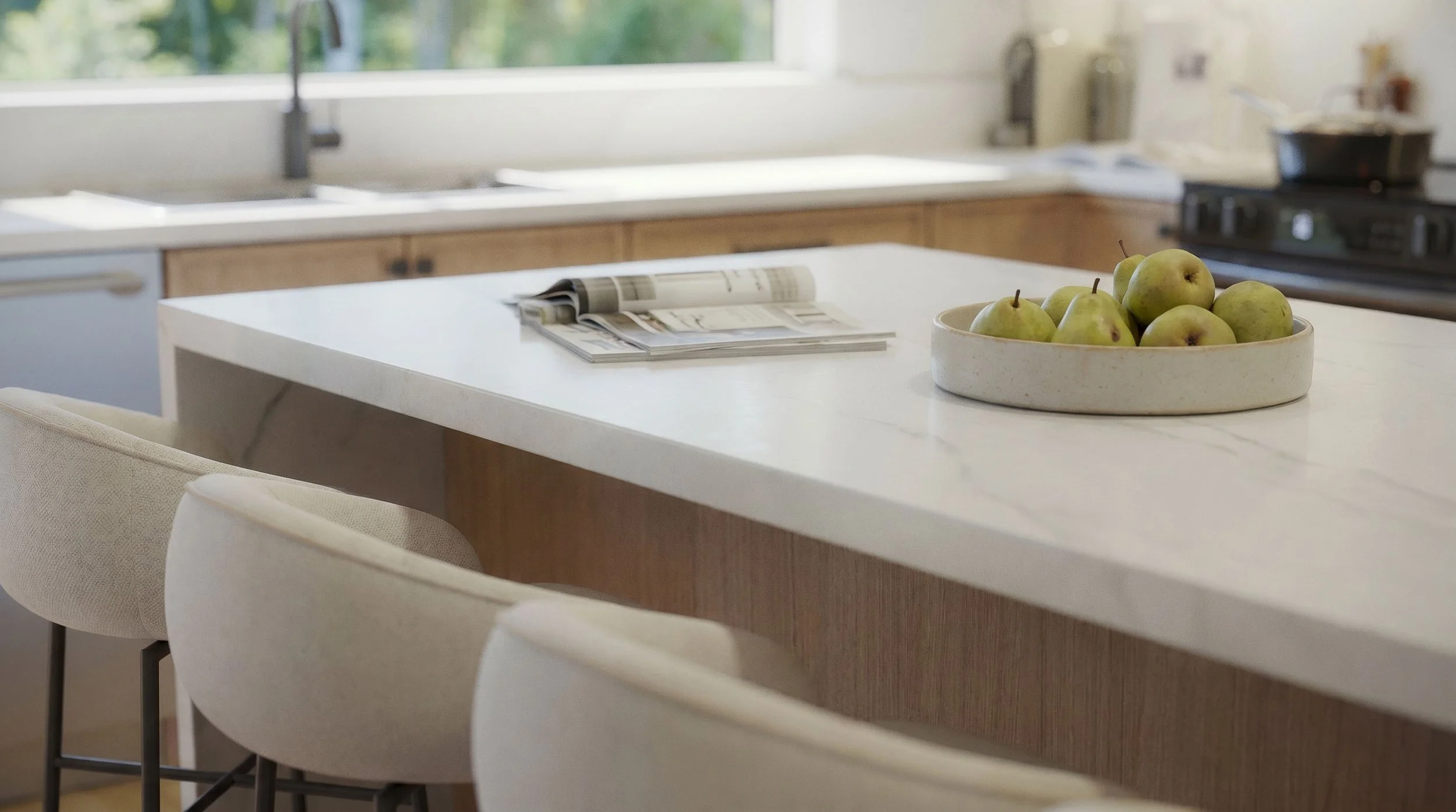 Kitchen with white island, bowl of green apples, open magazine, beige chairs, wooden cabinets, window, and stove.