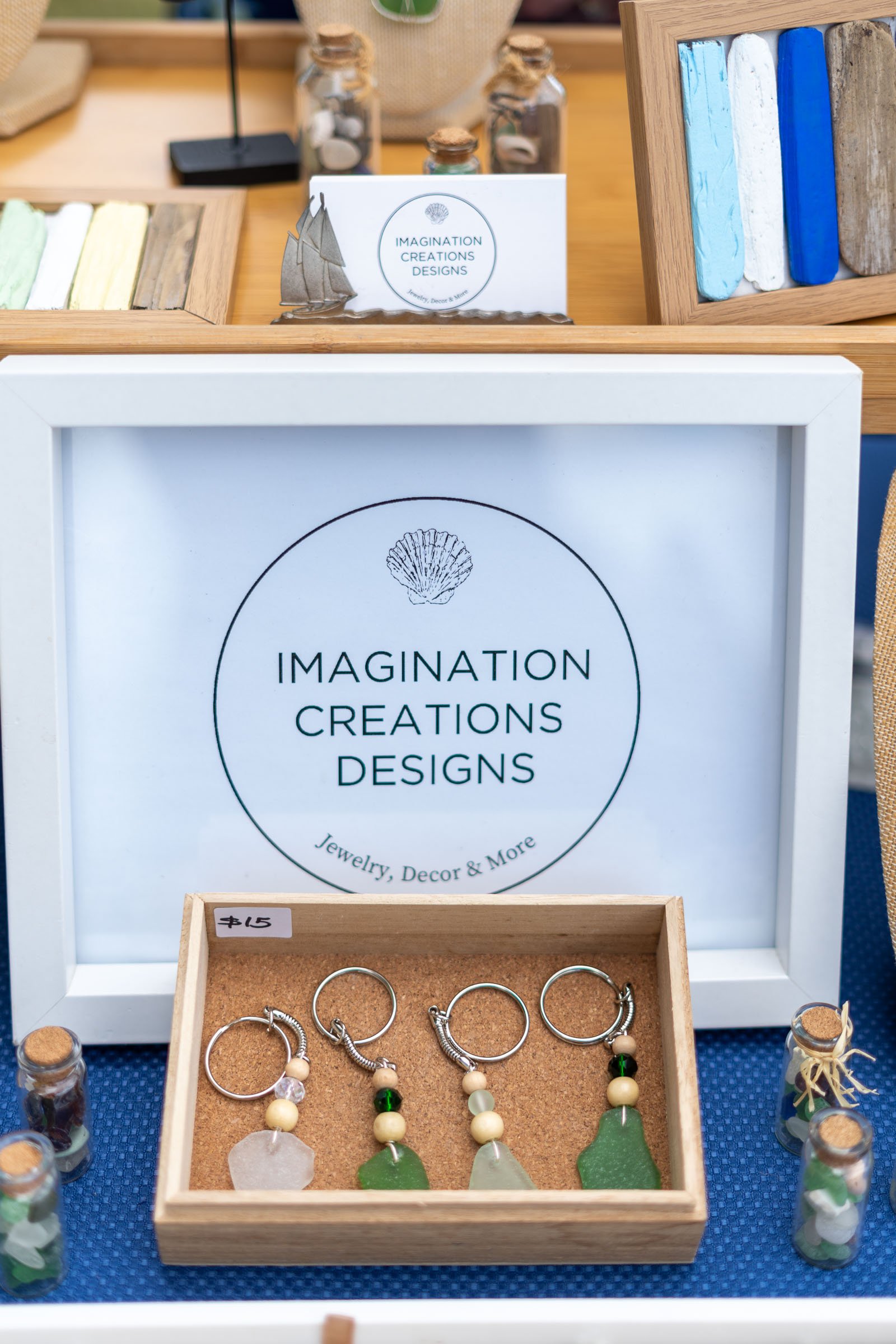 Jewelry display with sea glass earrings, a small wooden box with a $15 price tag, and small bottles filled with decorative stones on a blue surface.