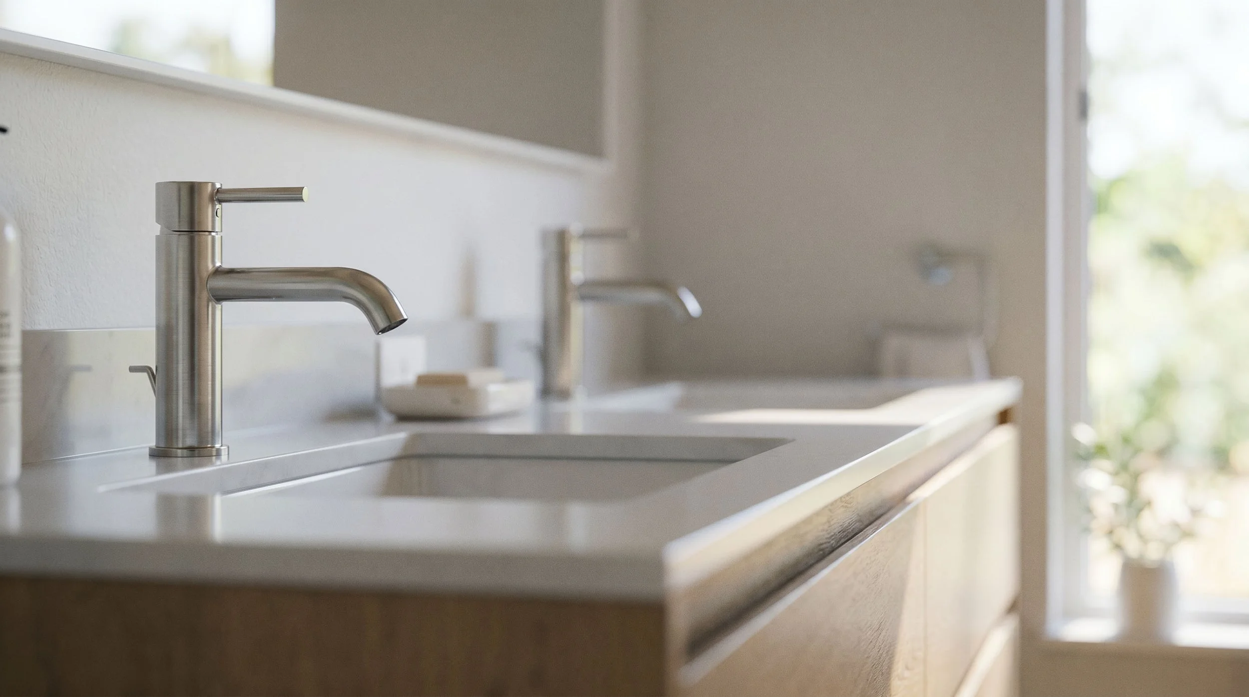 Modern kitchen with stainless steel faucet, white counter, and natural light from window.