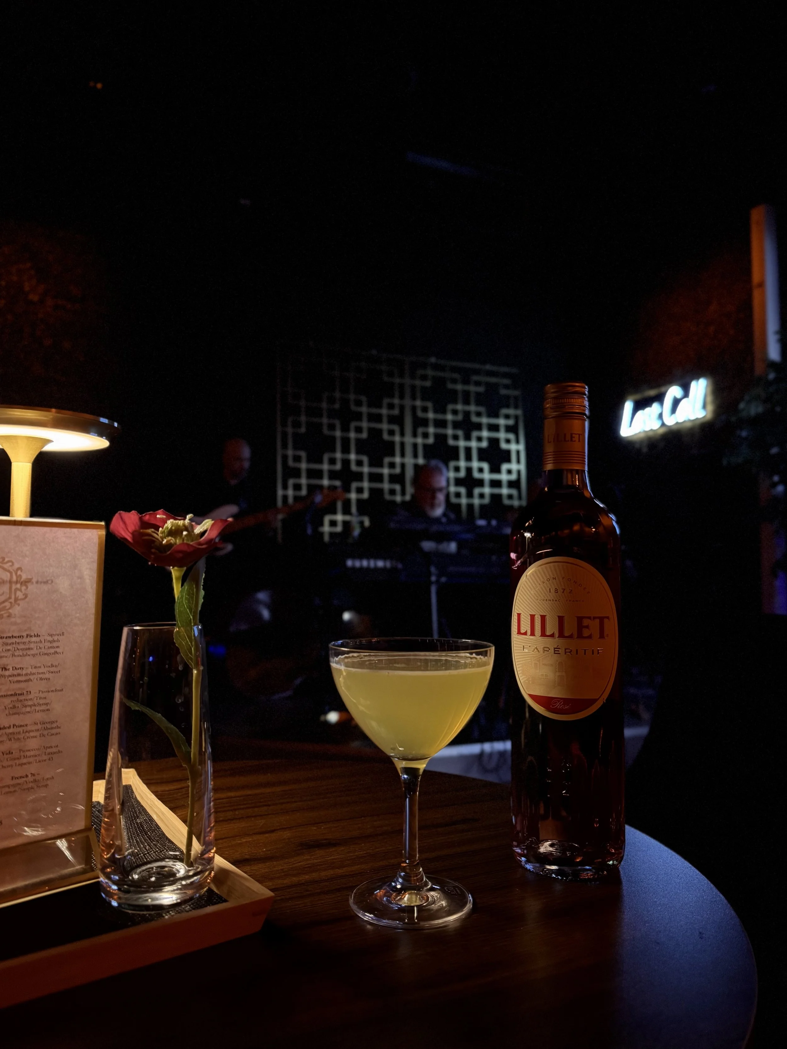 A cocktail and aperitif bottle on a table, in front of the live music stage