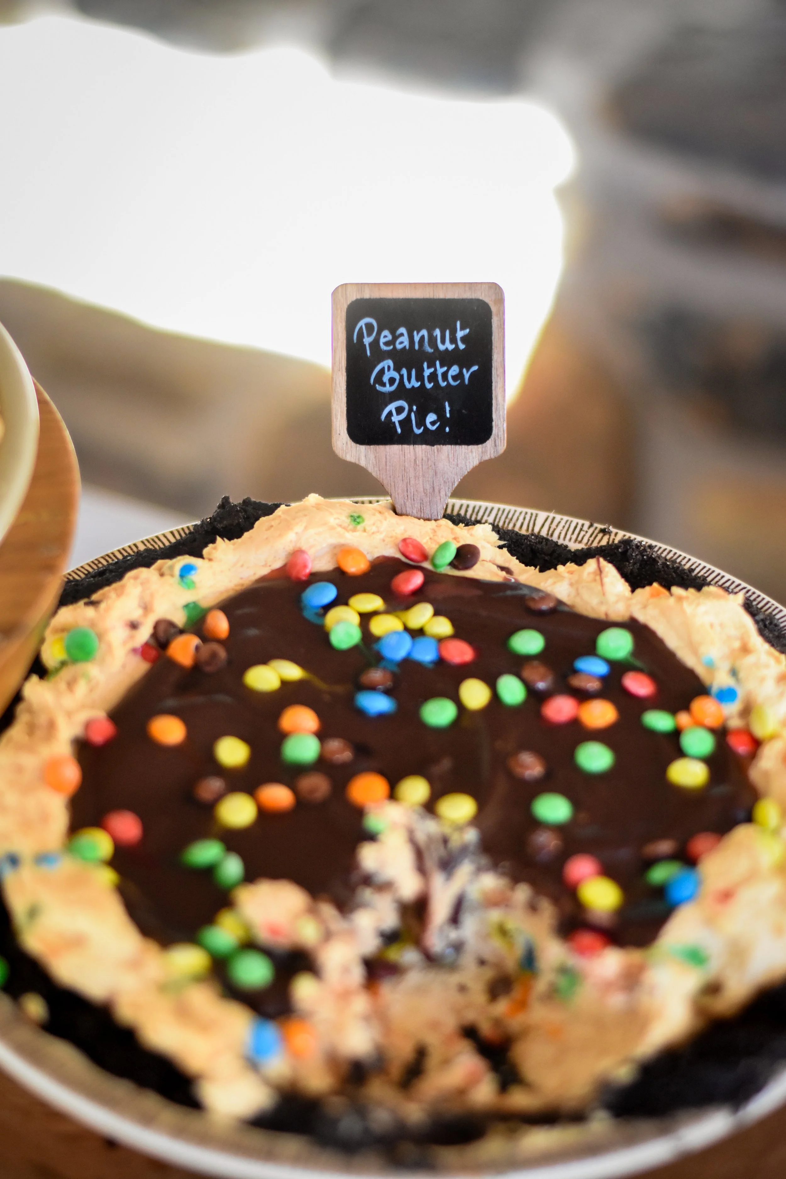 A chocolate pie topped with colorful sprinkles and a small chalkboard sign reading 'Peanut Butter Pie'.