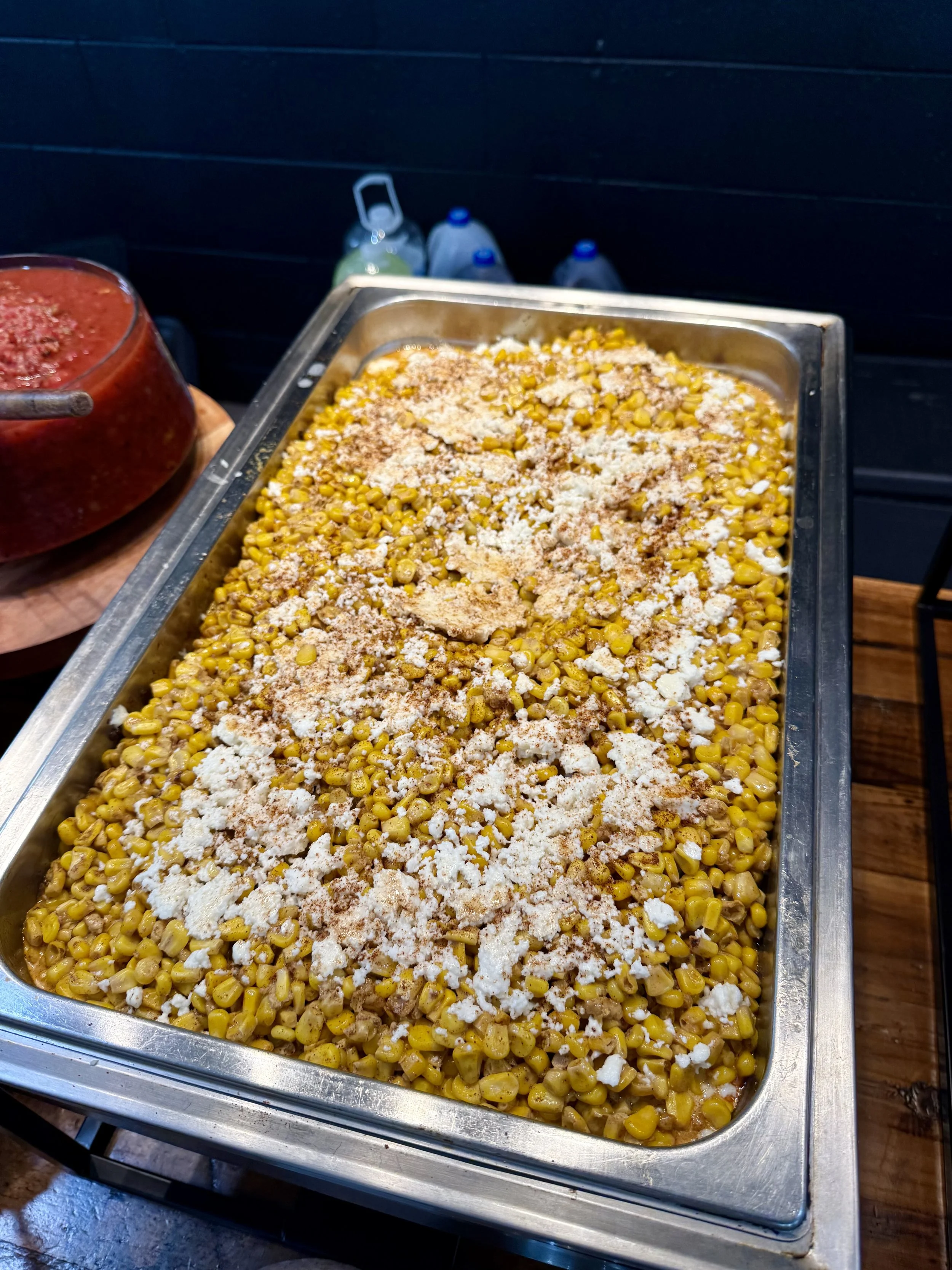 Tray of cooked yellow corn with white cheese and seasonings on top.