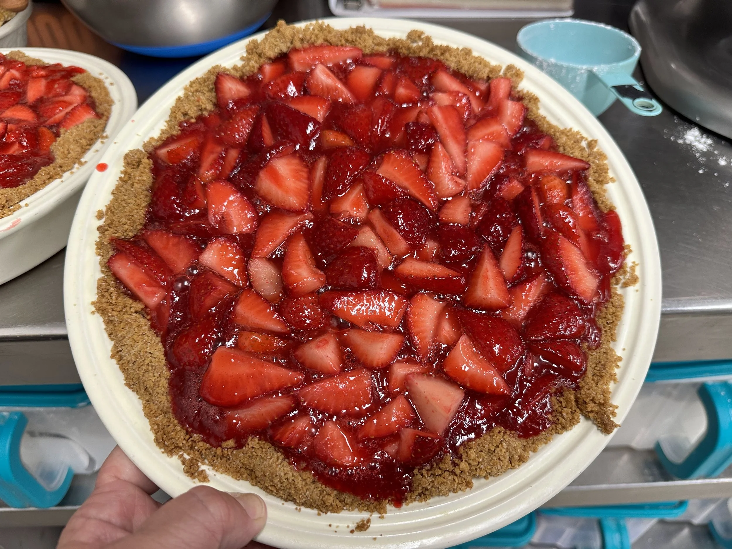 A strawberry pie with a graham cracker crust and a filling topped with sliced strawberries and a red glaze.