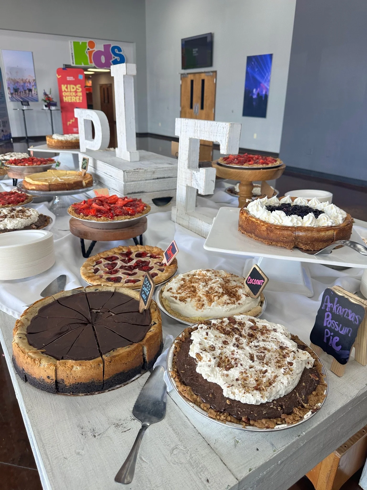 Assorted cakes and pies on a table at a buffet or party, including chocolate, fruit, and cream-topped desserts.
