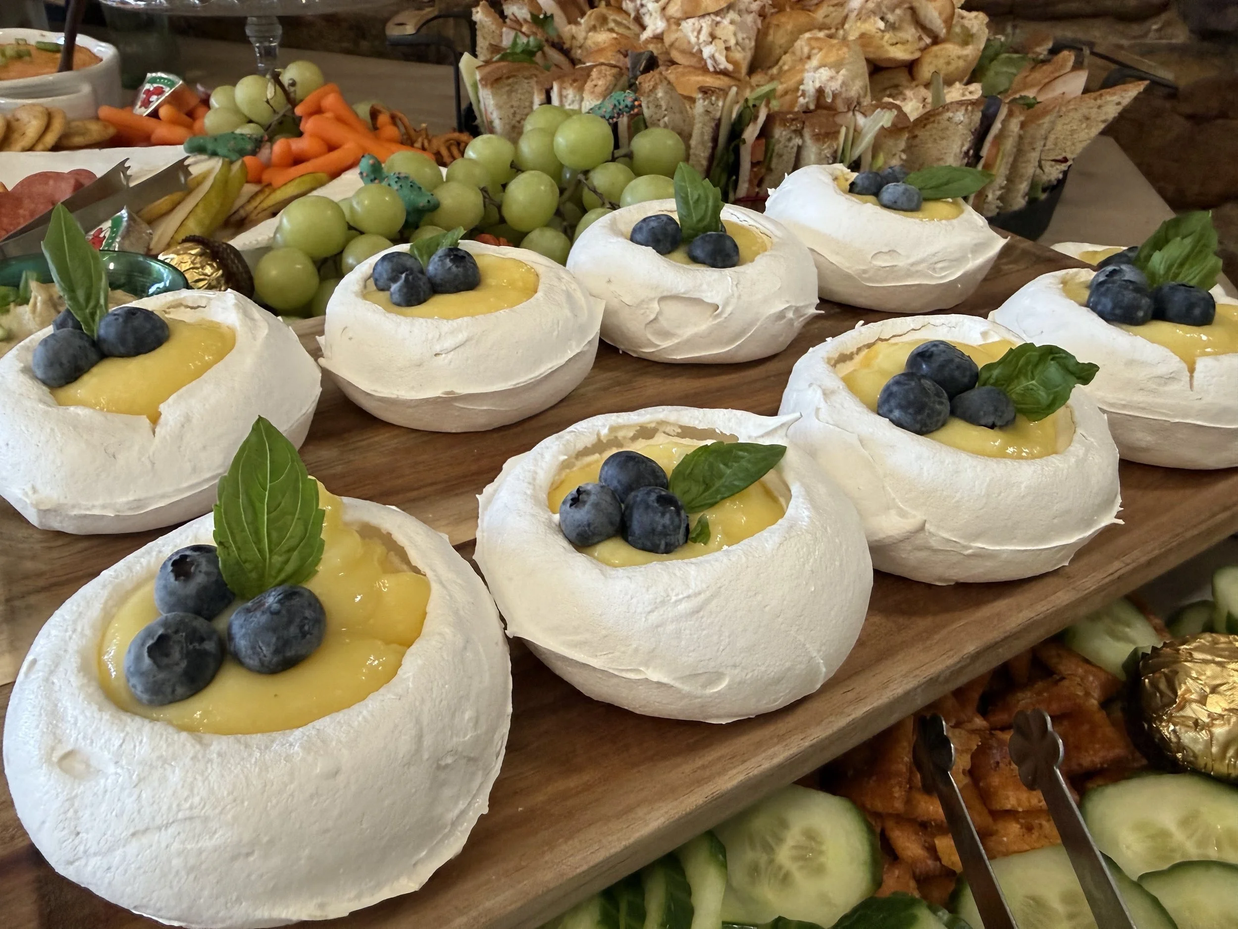 Brie cheese cups topped with blueberries and basil leaves, set on a wooden platter at a party.