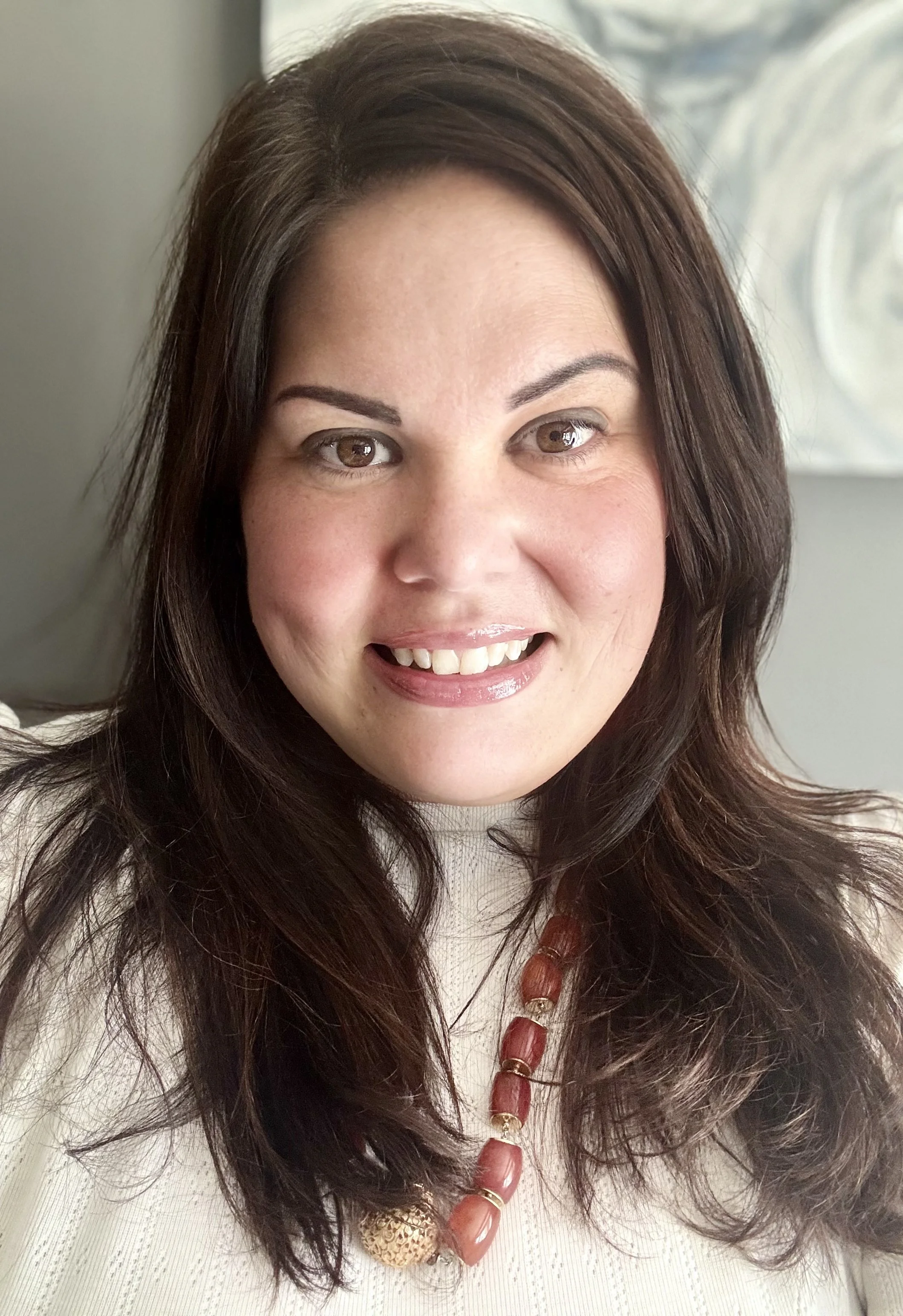 Jenny Mahn, Reiki Master, smiling in a white shirt with dark brown hair in front of a gray wall