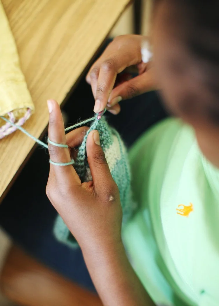 A person knitting with green yarn at a wooden table.