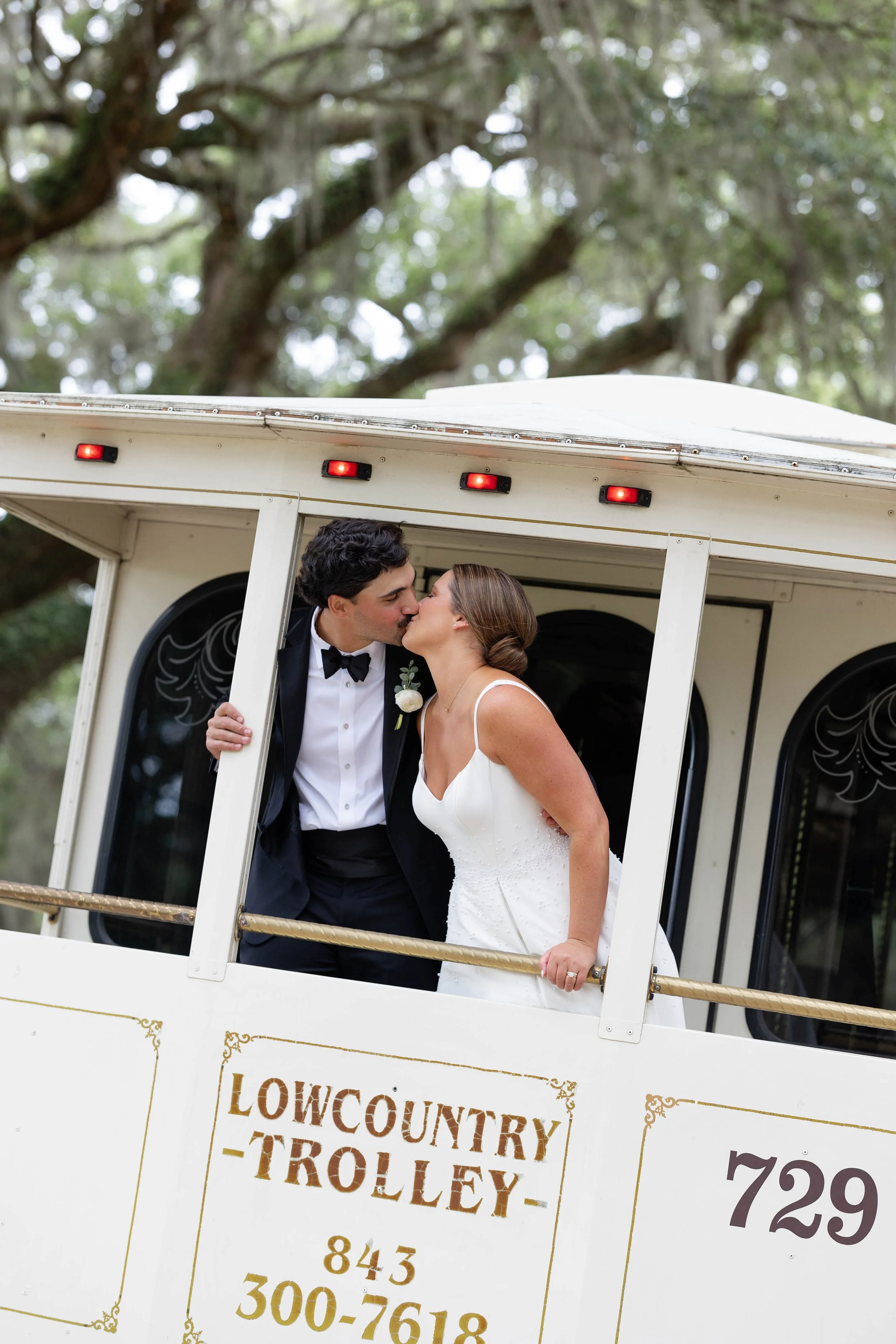A bride and groom kissing on a Lowcountry Trolley, with trees in the background.