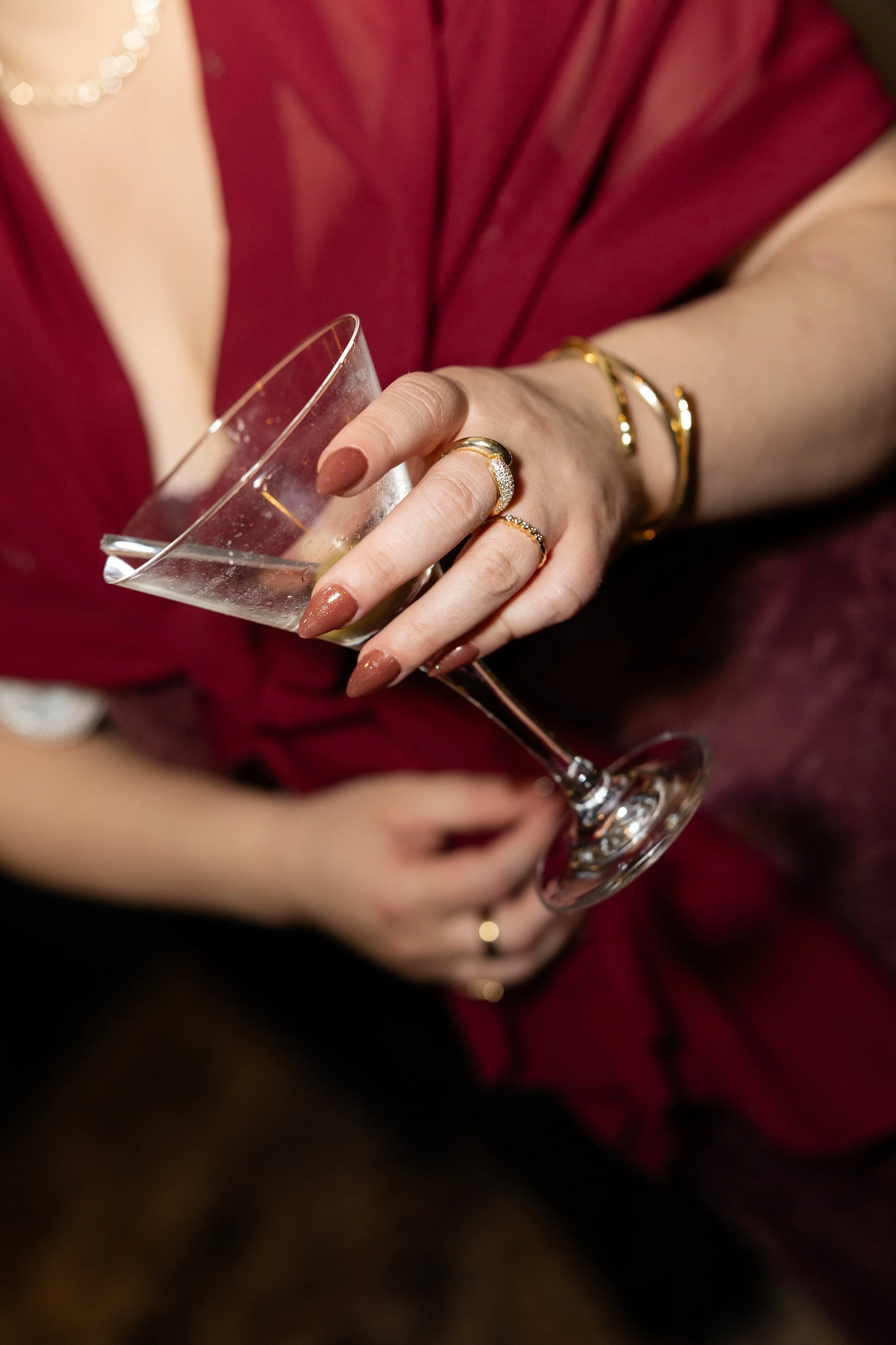 Close-up of a woman wearing gold jewelry, holding an empty champagne flute, wearing a red dress.