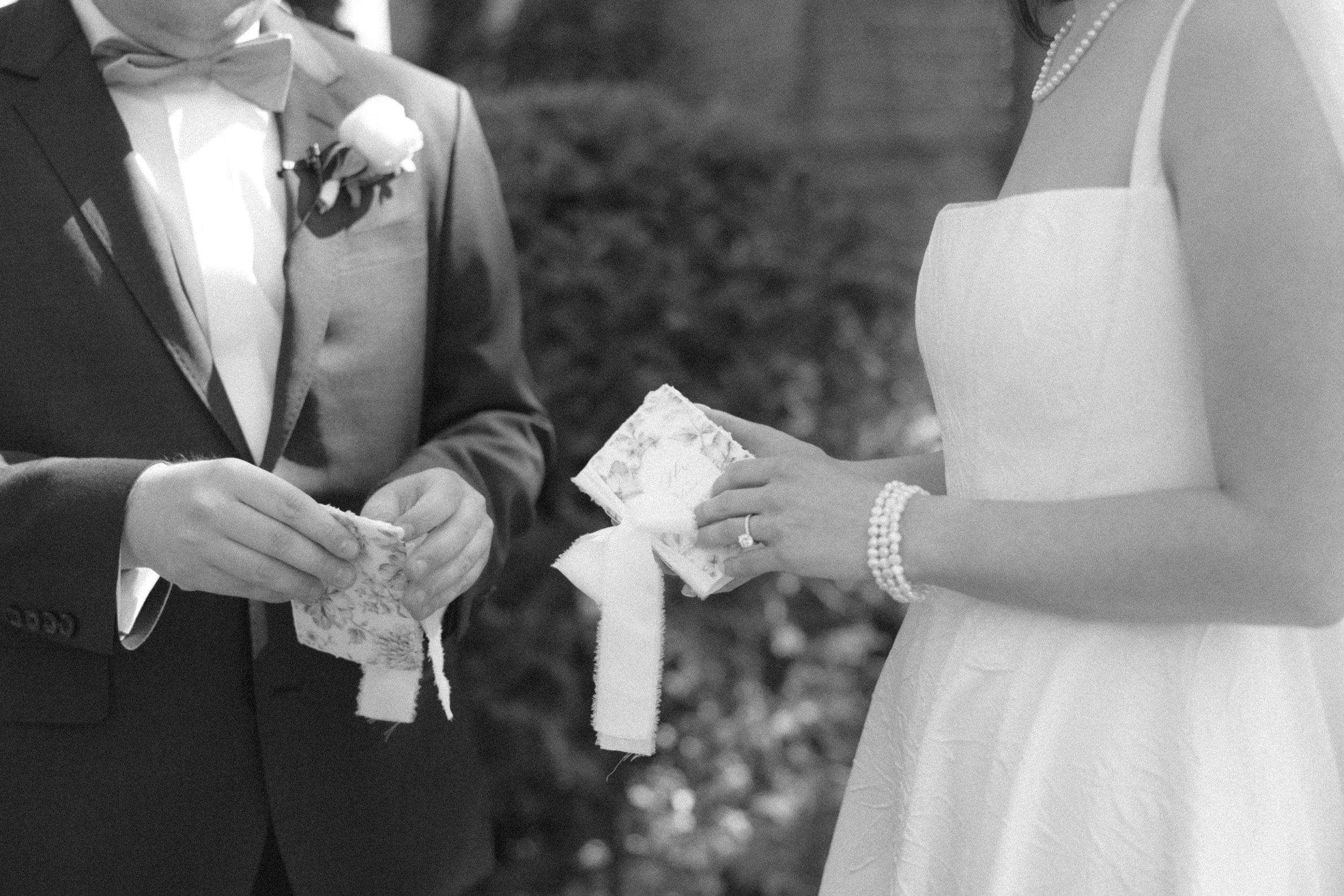 Wedding ceremony with a bride and groom exchanging rings, both dressed in formal wedding attire, with the groom in a suit and bow tie and the bride in a wedding dress and pearl jewelry.