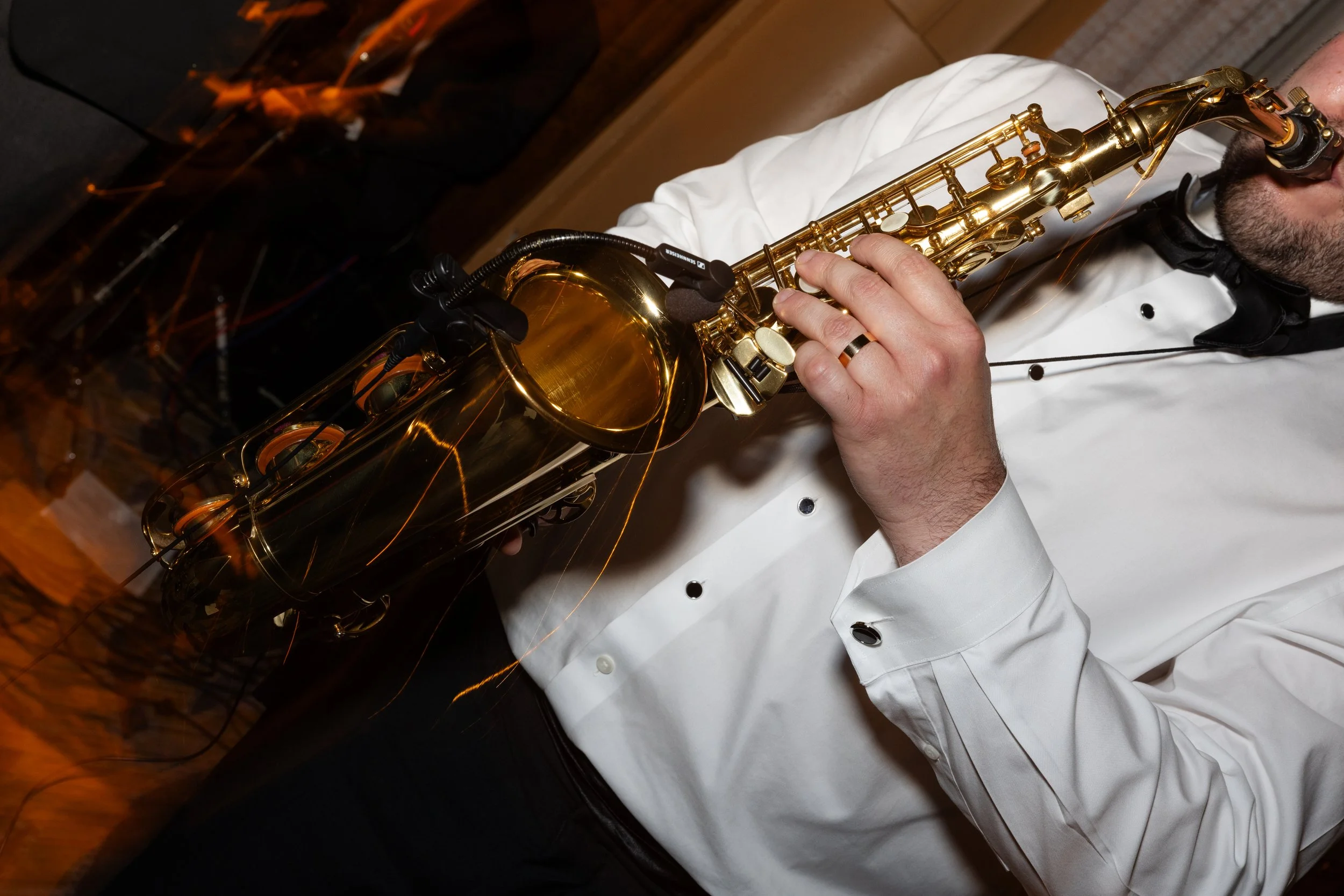 A man in a white chef coat playing a gold saxophone in a cozy indoor setting.