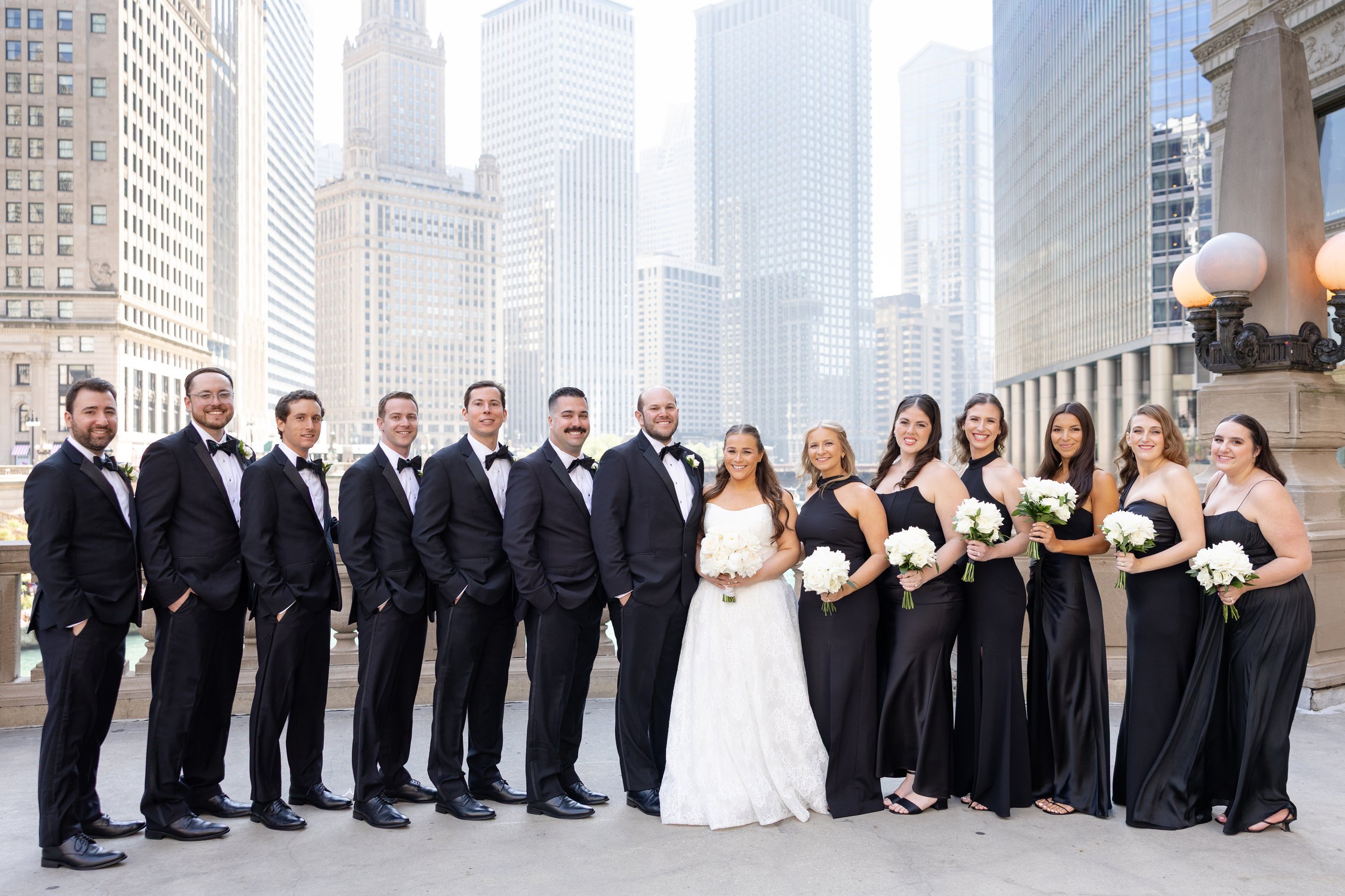 A group of bride and groom and bridesmaids and groomsmen posing on a city street, with tall buildings in the background.