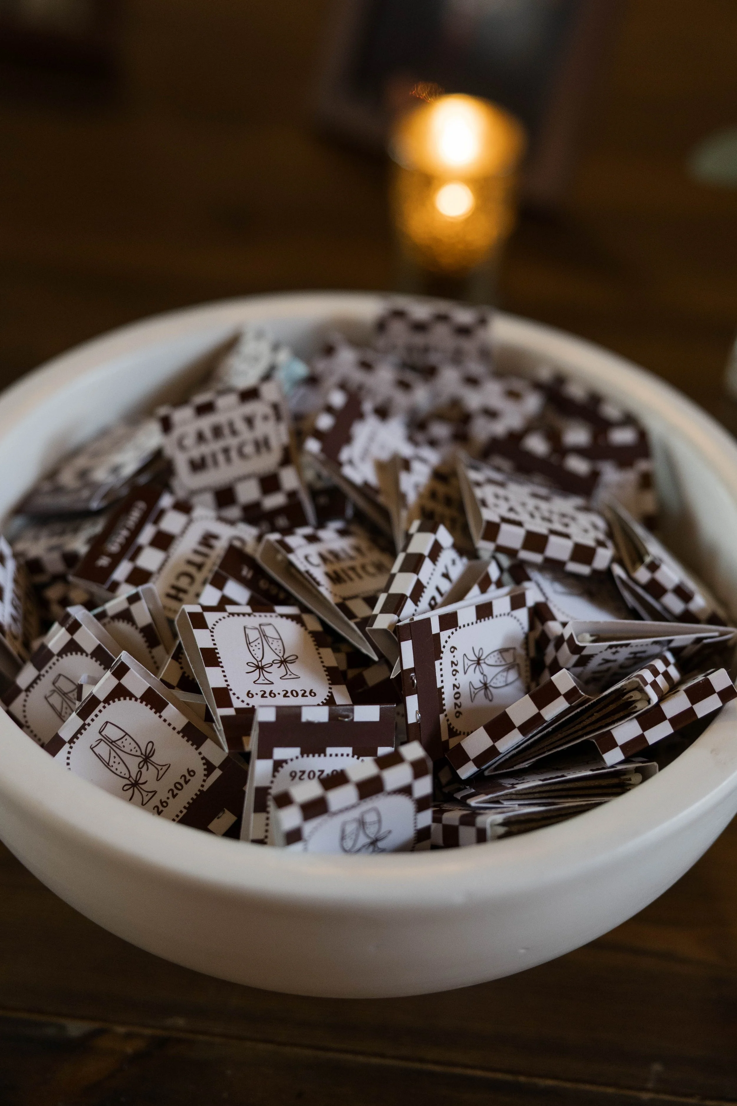 A white bowl filled with small folded paper favors with wedding icons and date '6-26-2026' printed on them.
