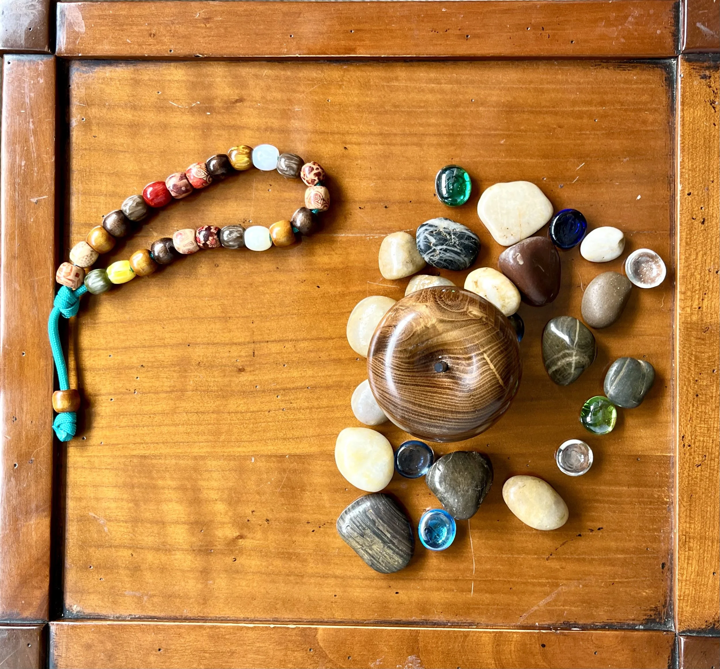Collection of colorful polished stones and beads on a wooden surface with a wooden frame.