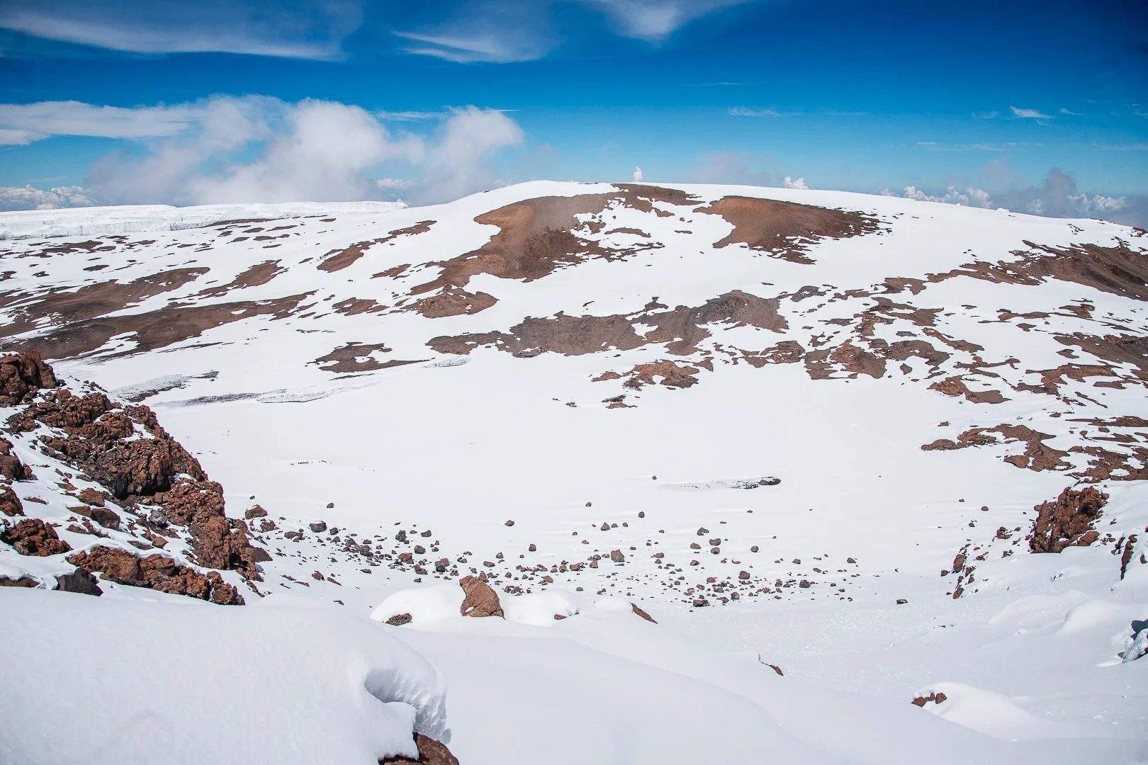 Snow-covered mountain with patches of exposed rock and a partly cloudy sky.