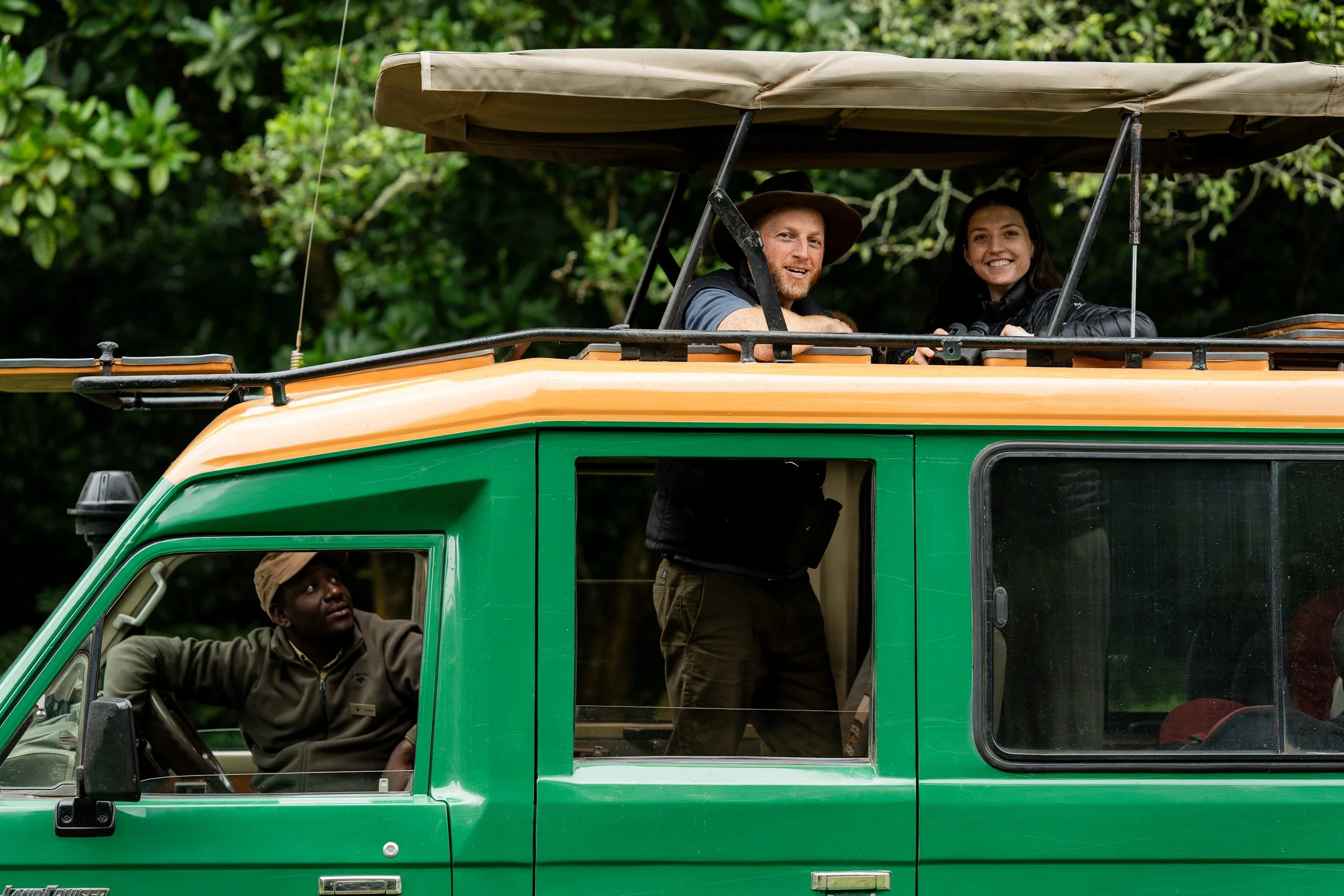 Couple of game drive in green car with a man in a cap driving who is the guide