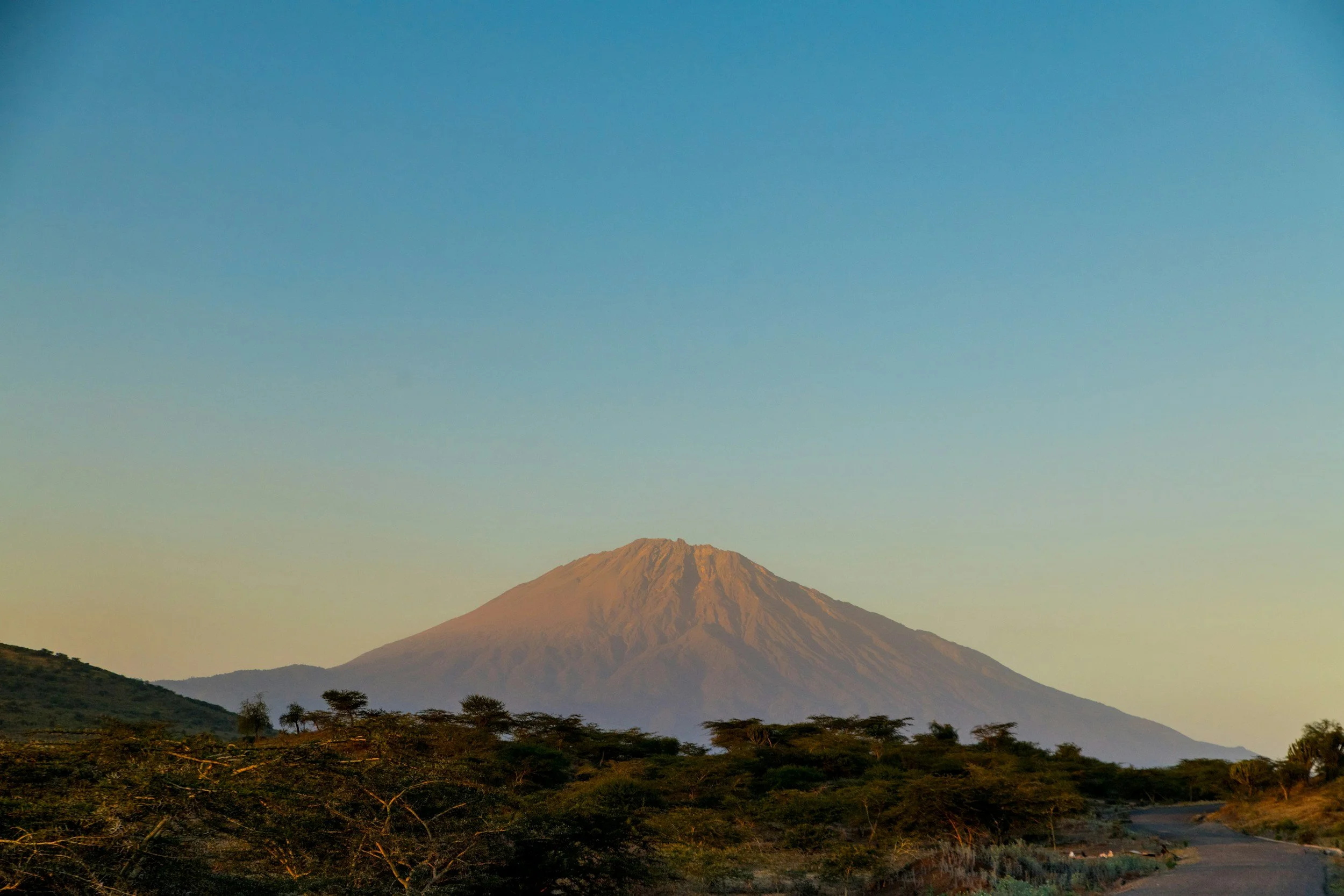 A mountain with a volcanic shape and a rugged peak, surrounded by green vegetation and a clear blue sky.
