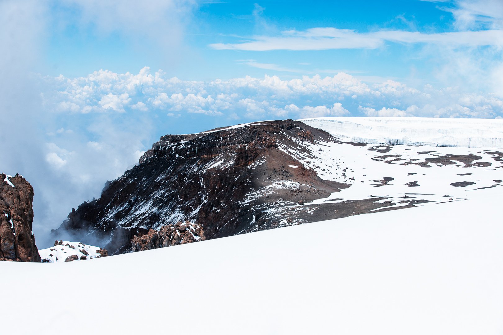 Snow-covered volcanic mountain with rocky terrain and a cloudy sky.