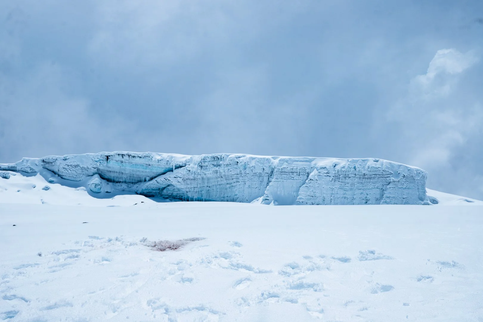 Large ice formation in a snowy landscape under a cloudy sky.